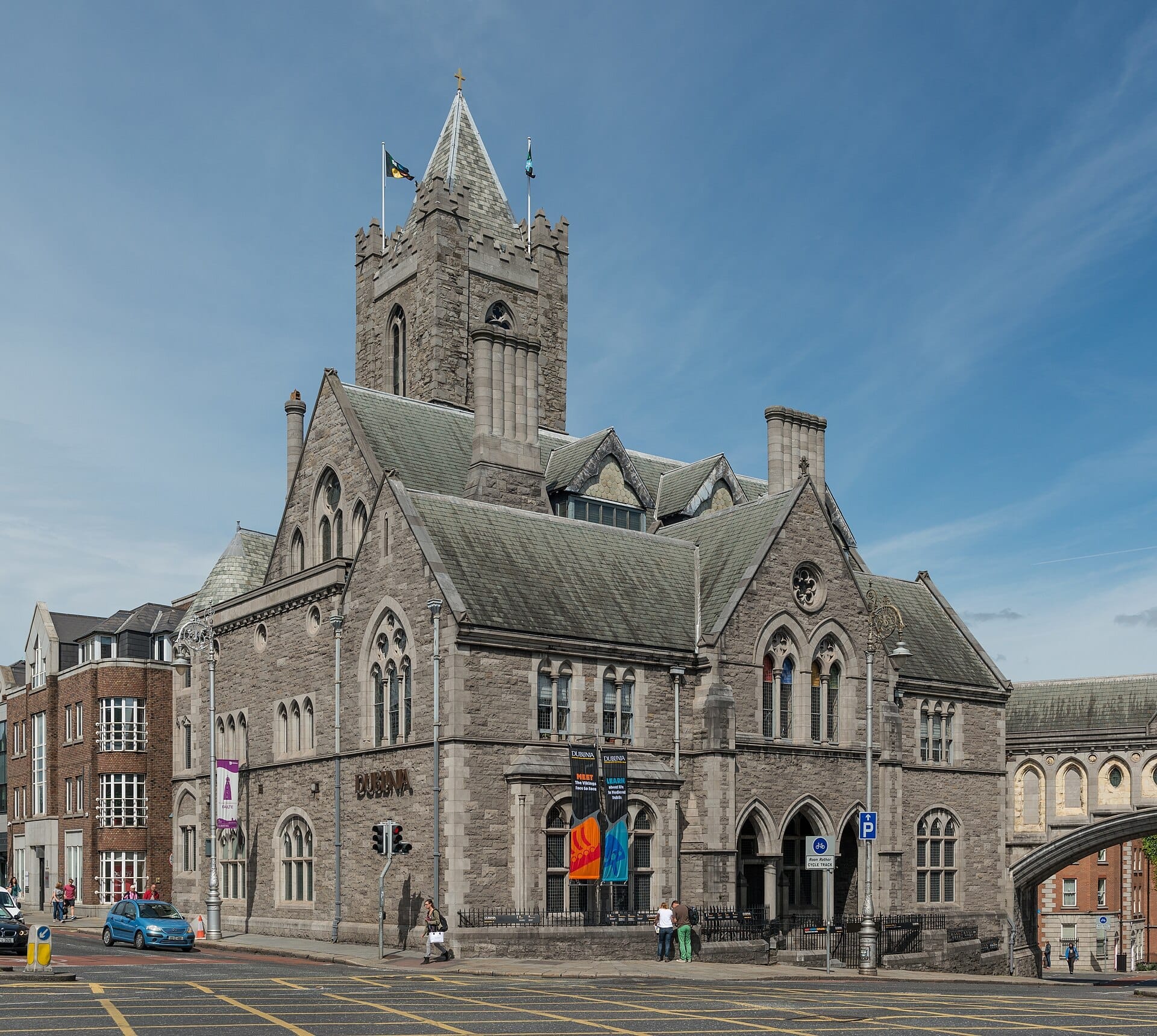 Vista esterna del museo Dublinia, ospitato in un grandioso edificio in stile neogotico, con archi in pietra, torre, colorati stendardi e un cielo azzurro limpido.