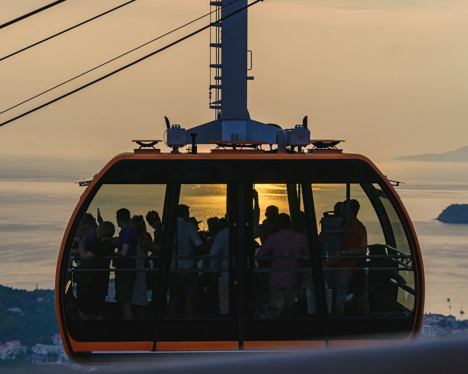 Primer plano del teleférico de Dubrovnik lleno de personas al atardecer, cables aéreos y mar Adriático al fondo.