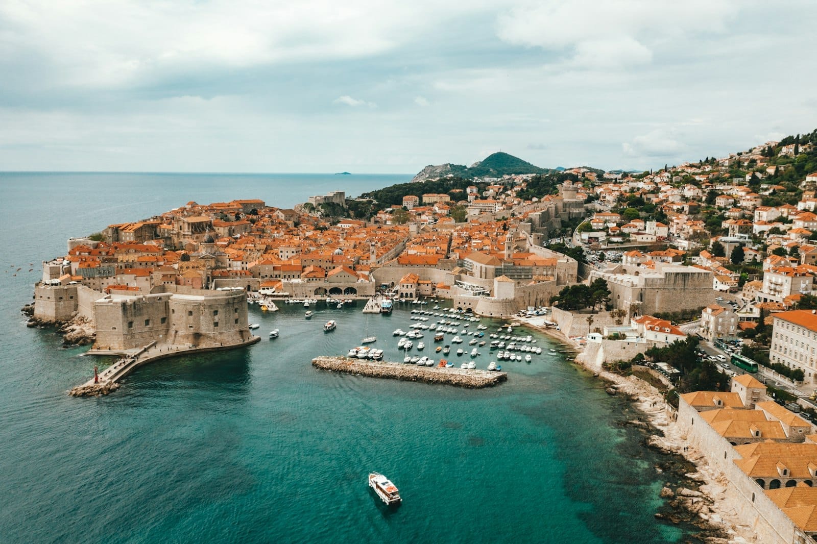 Vista aérea del Casco Antiguo de Dubrovnik con sus murallas históricas, el puerto lleno de embarcaciones y el azul intenso del mar Adriático, ideal para viajeros de crucero.
