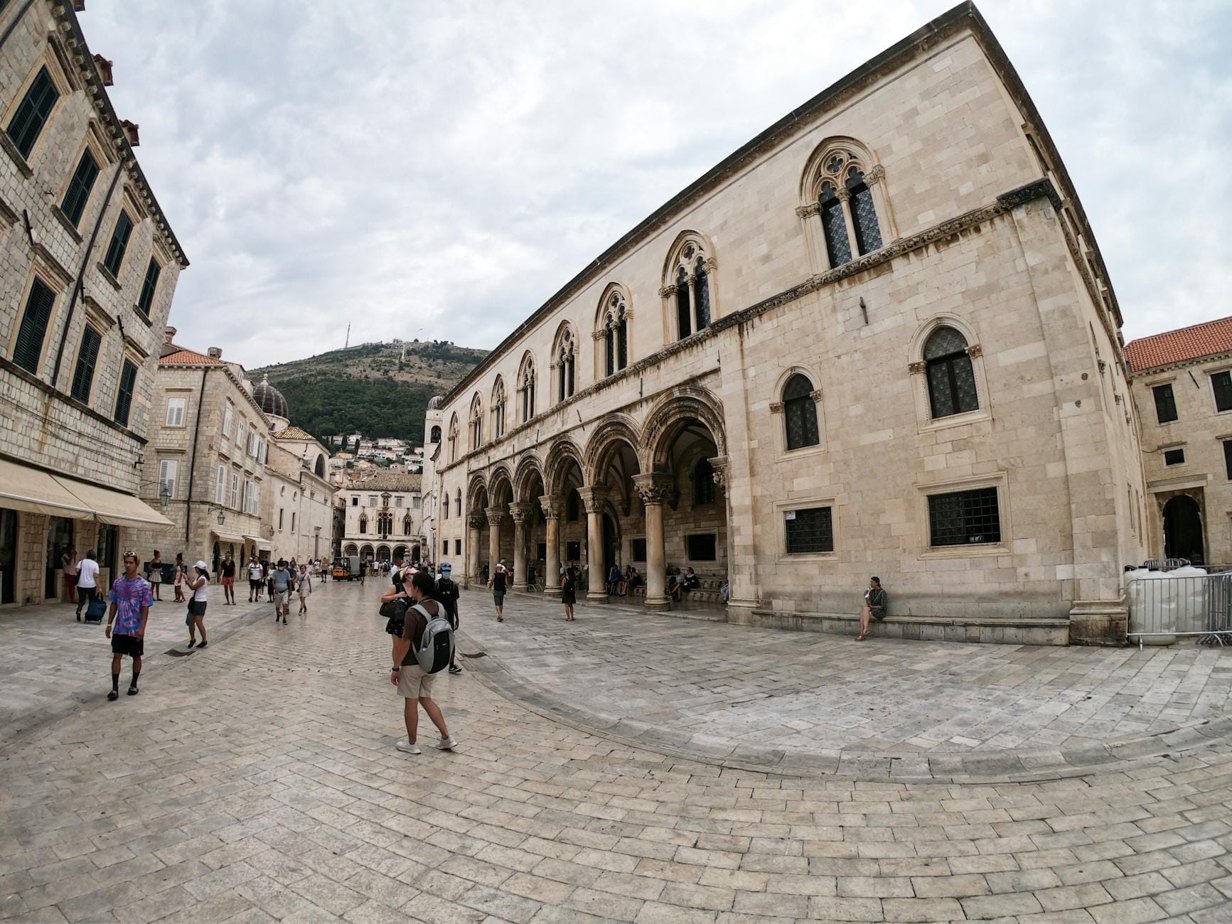 Des personnes marchant devant un élégant bâtiment en pierre avec des arches dans la vieille ville de Dubrovnik, mettant en valeur l'architecture historique juste à l'intérieur des remparts.