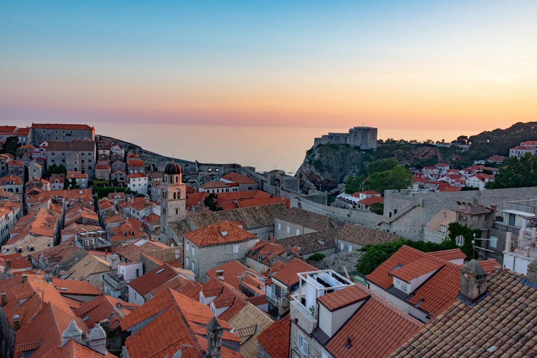 Vista romántica del atardecer sobre las murallas y tejados del casco antiguo de Dubrovnik con el mar al fondo.