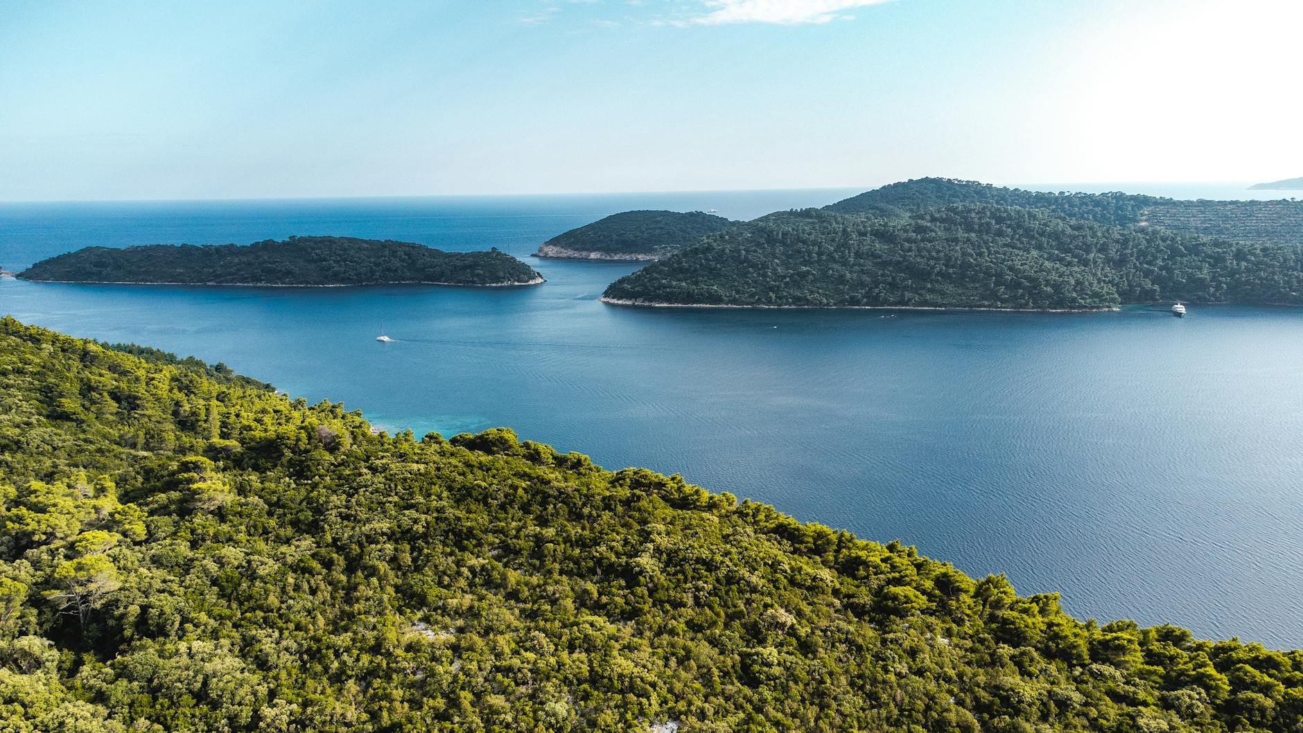 Vue aérienne de trois îles verdoyantes entourées d'une mer bleue cristalline près de Dubrovnik sous un ciel lumineux.