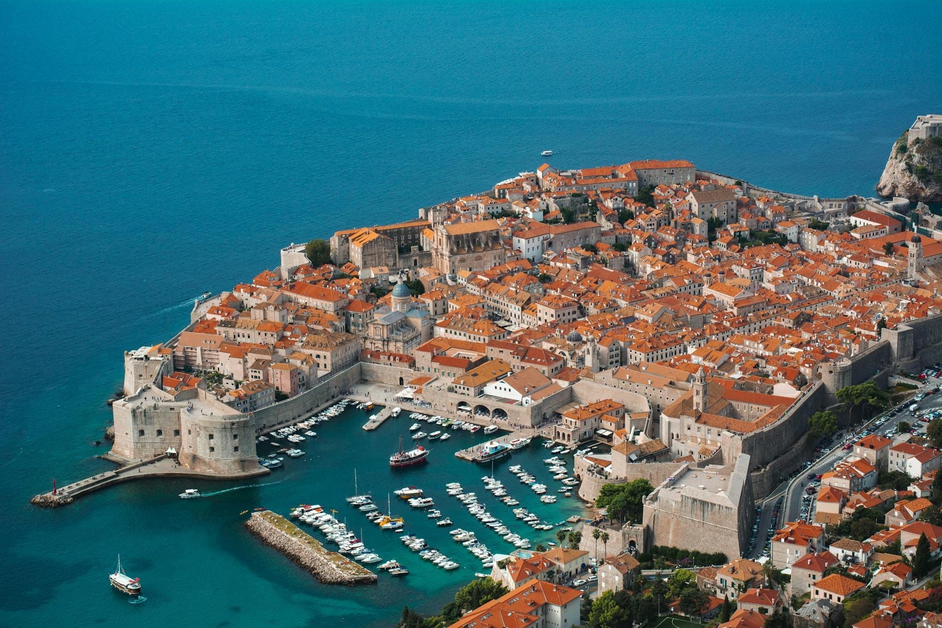 Vista aérea del casco antiguo amurallado de Dubrovnik y su puerto deportivo rodeados por el vívido azul del mar Adriático en un día soleado.