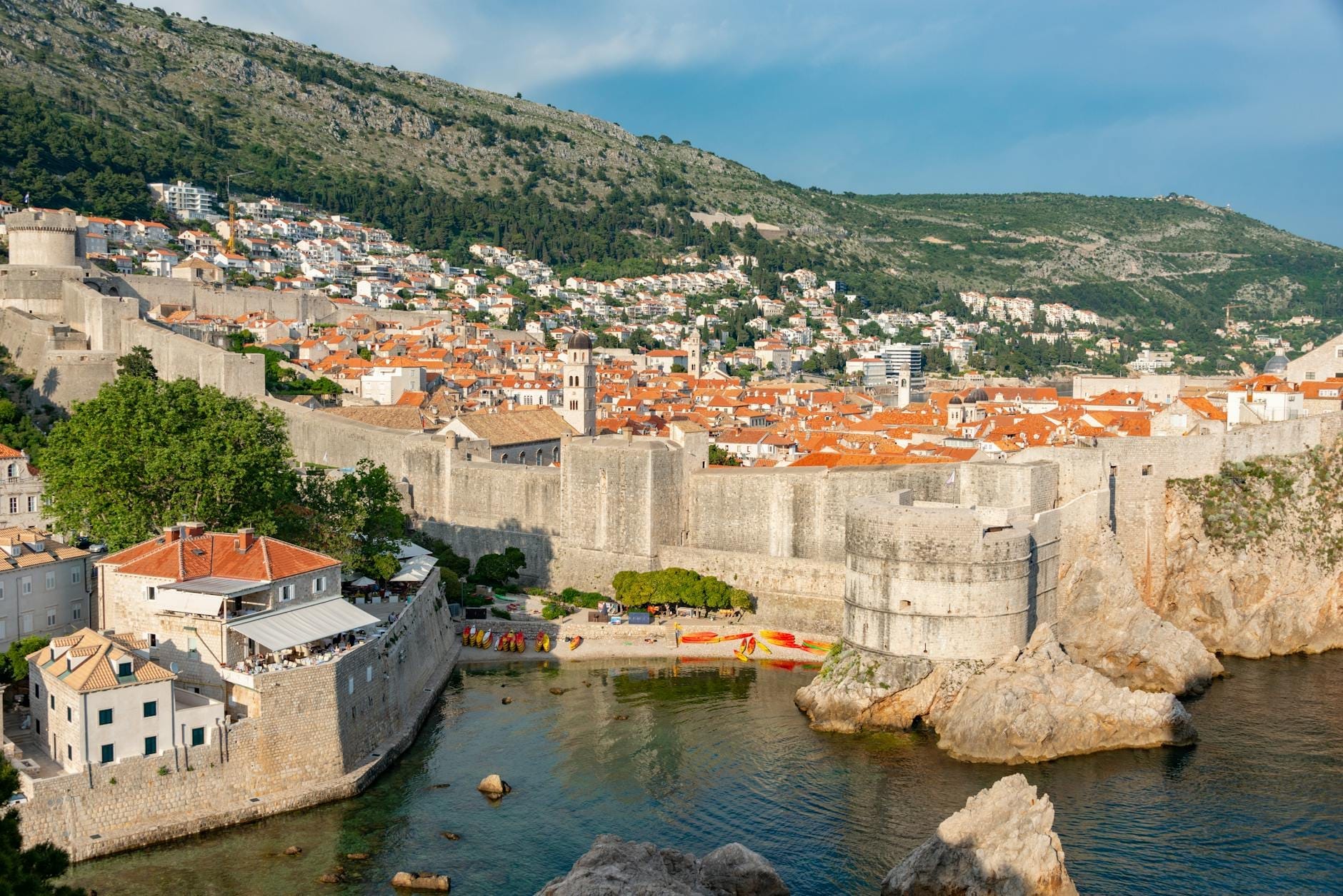 Vue panoramique des remparts de Dubrovnik avec ses tourelles et ses bâtiments aux toits rouges de la vieille ville nichés contre une colline, surplombant la mer Adriatique.