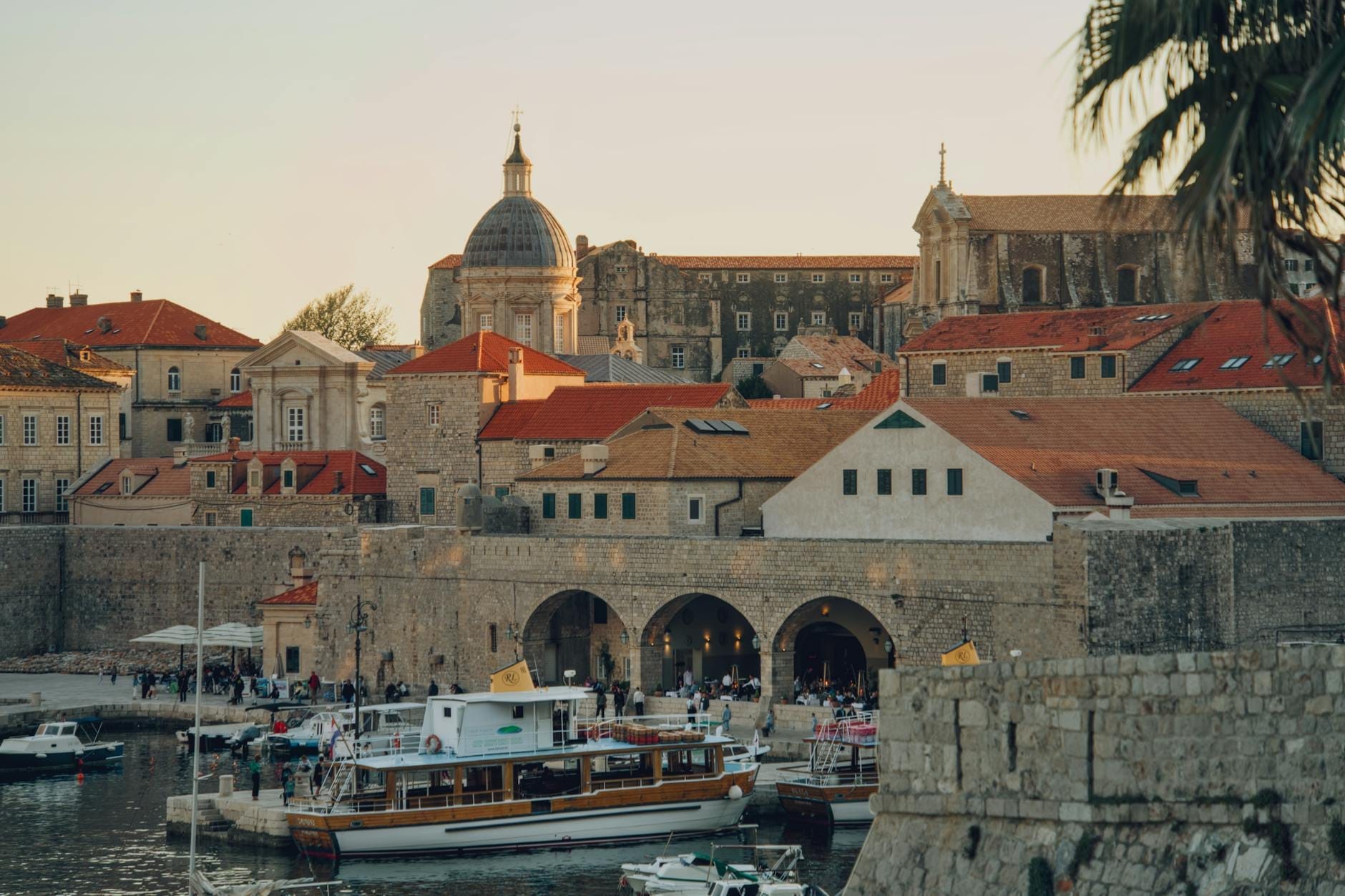 Port de Dubrovnik avec des bateaux, des remparts en pierre et des bâtiments historiques au coucher du soleil, illustrant les transports et l'atmosphère locale.