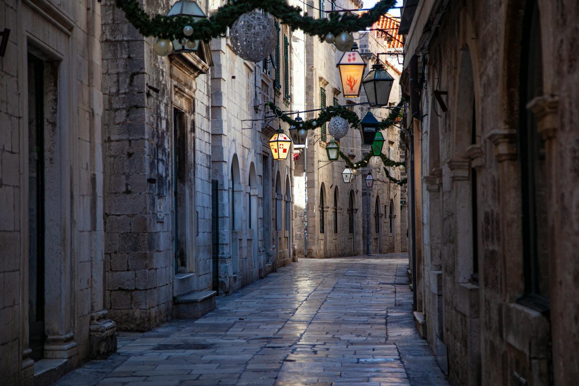 Hẻm đá hẹp vắng người ở phố cổ Dubrovnik được trang trí bằng đèn lồng và vòng hoa treo.