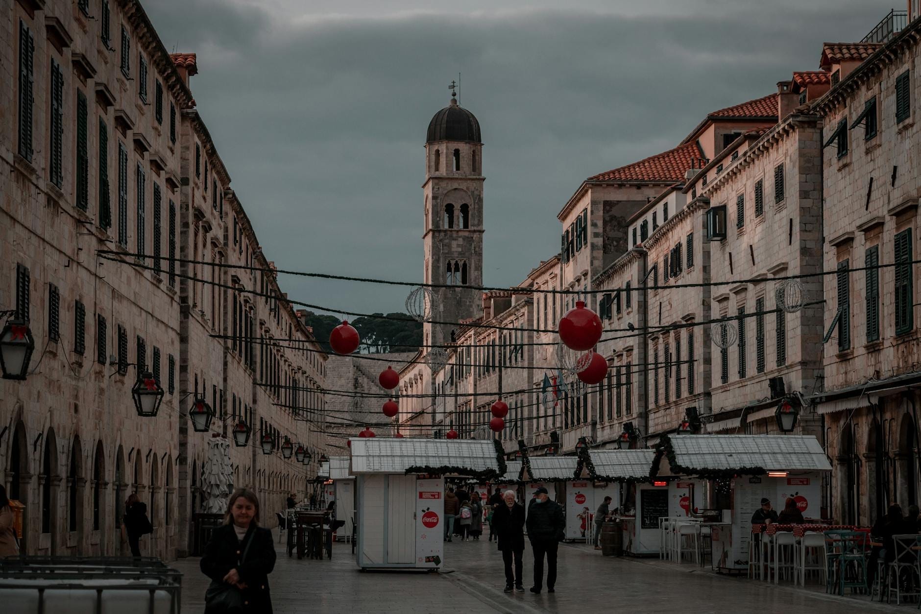 La rue principale de Dubrovnik avec des décorations de fêtes hivernales, quelques personnes qui se promènent, un ciel couvert et des bâtiments historiques dans la vieille ville.