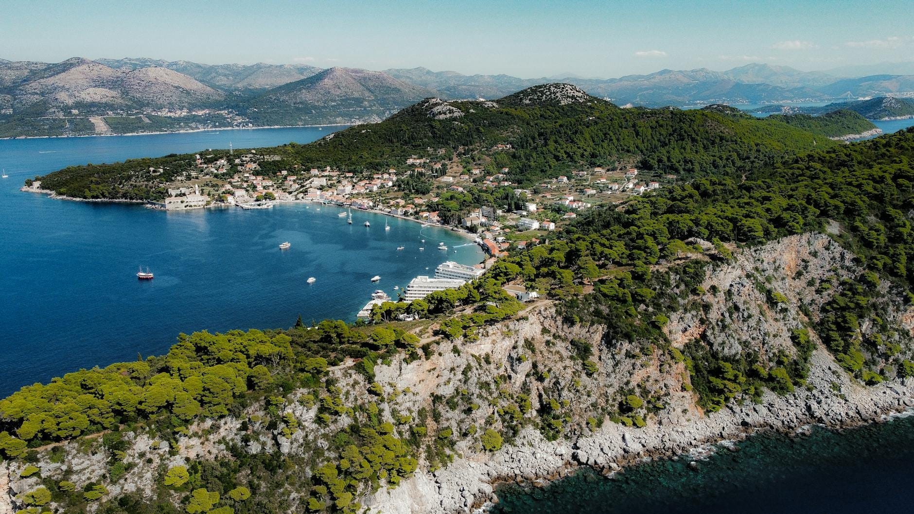Dubrovnik yakınlarındaki yemyeşil bir adanın küçük bir köy, plajlar ve berrak mavi denizdeki teknelerle havadan görünümü.