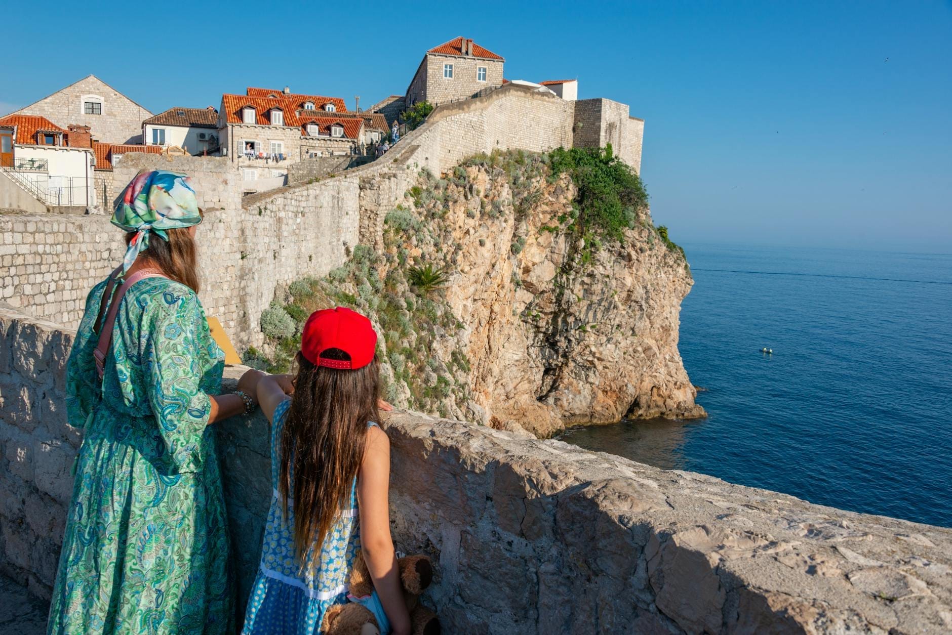 İki çocuk, açık ve güneşli bir günde Dubrovnik şehir surlarından denize ve eski tahkimatlara bakıyor.