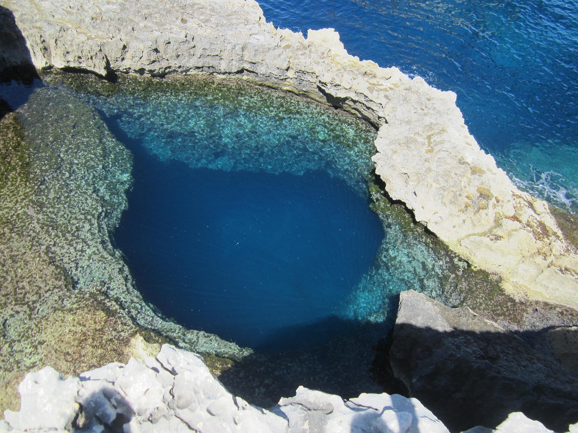 Vista dall'alto del Blue Hole a Dwejra, Gozo, con acque blu cristalline circondate da aspre formazioni calcaree.
