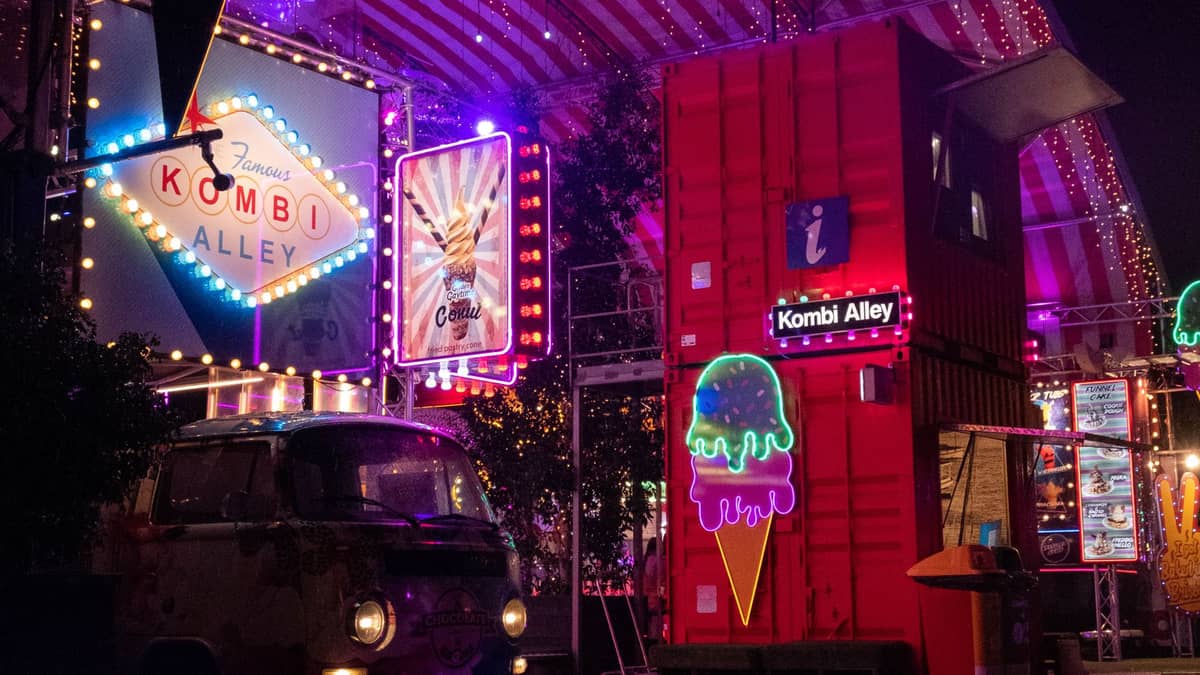 Eat Street Northshore at night showing neon-lit Kombi Alley, red shipping containers, colorful signage, and vibrant market atmosphere.