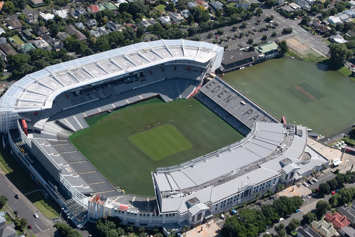 Luftaufnahme des Eden Park Stadions in Auckland mit seinen Tribünen, dem grünen Spielfeld, dem angrenzenden Cricketplatz und dem umliegenden Wohnviertel an einem sonnigen Tag.