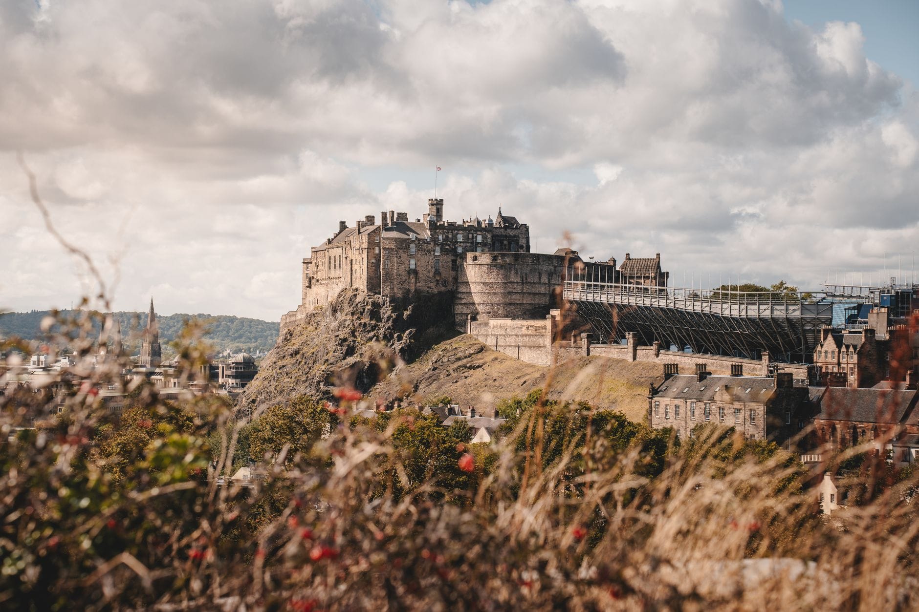 Weite Landschaftsaufnahme von Edinburgh Castle auf seinem Vulkanfelsen, die Skyline beherrschend – mit dramatischen Wolken und Vegetation im Vordergrund.