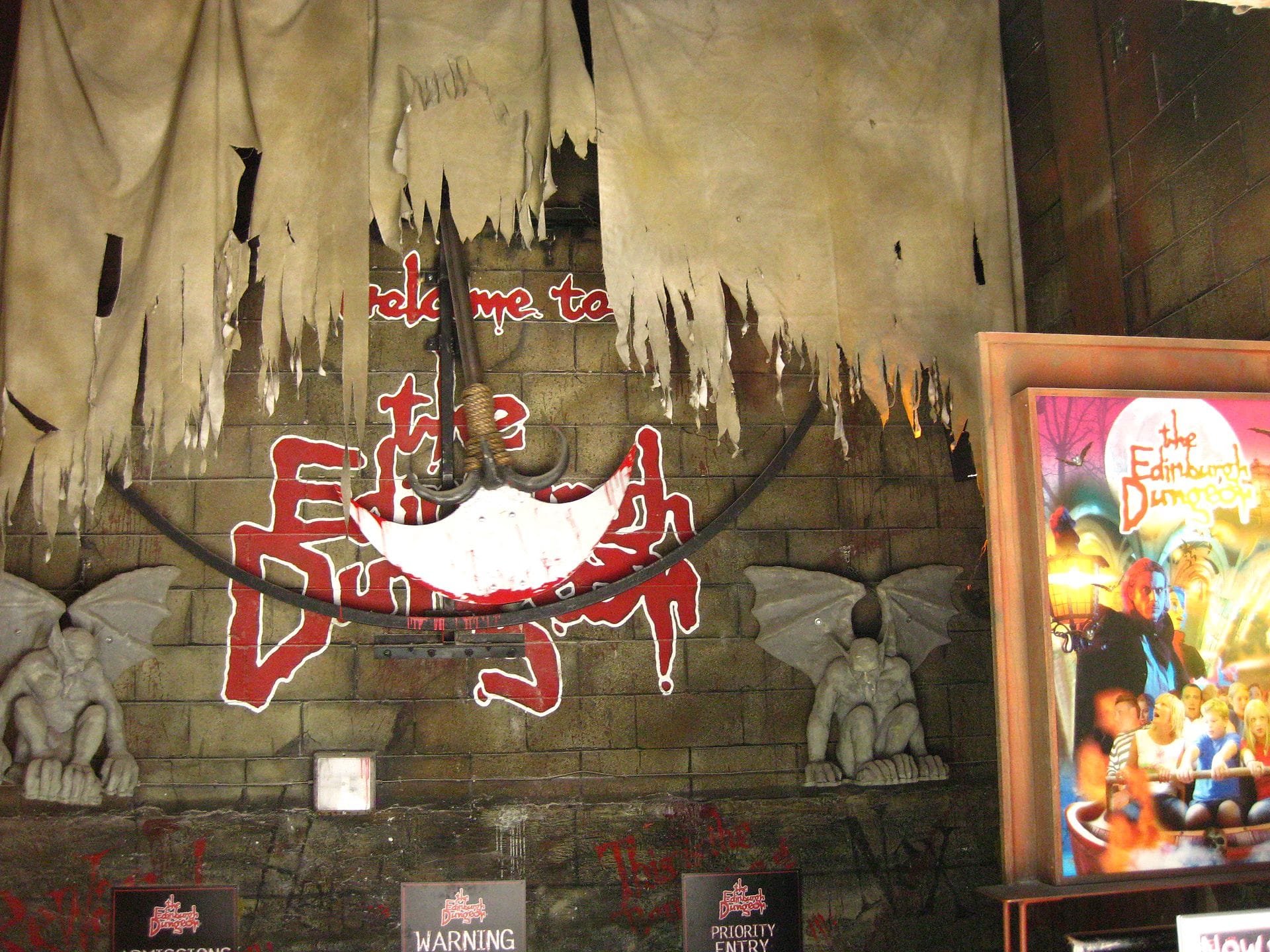 Eingangsbereich des Edinburgh Dungeon mit dramatischem Schild, riesiger falscher Axt, Gargoyle-Statuen und aufwendig gestalteter Themendekoration, die Besucher von Anfang an beunruhigen soll.
