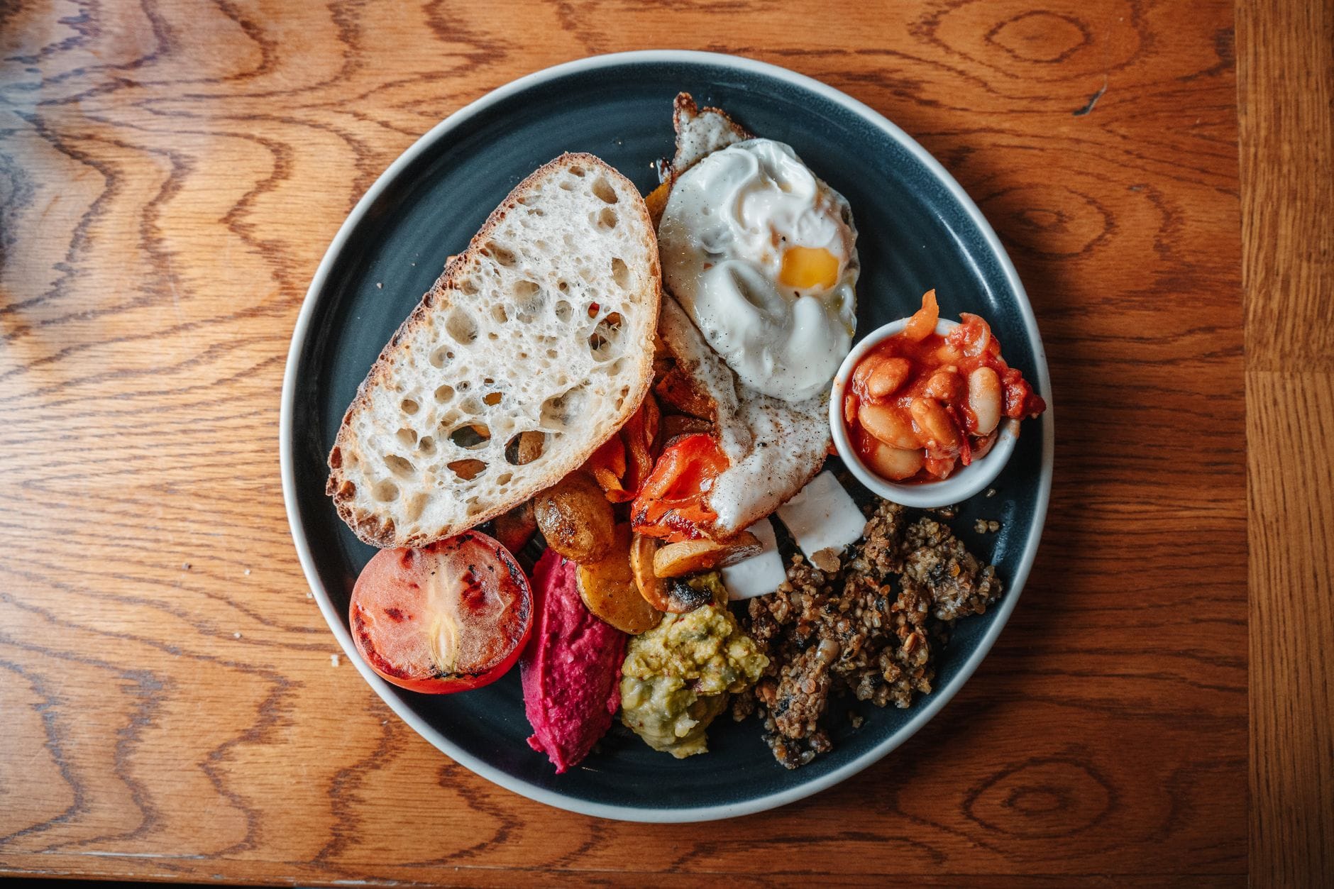 Talerz tradycyjnego szkockiego śniadania z haggis, fasolą, jajkiem sadzonym, chlebem, pomidorem i innymi dodatkami na drewnianym stole.