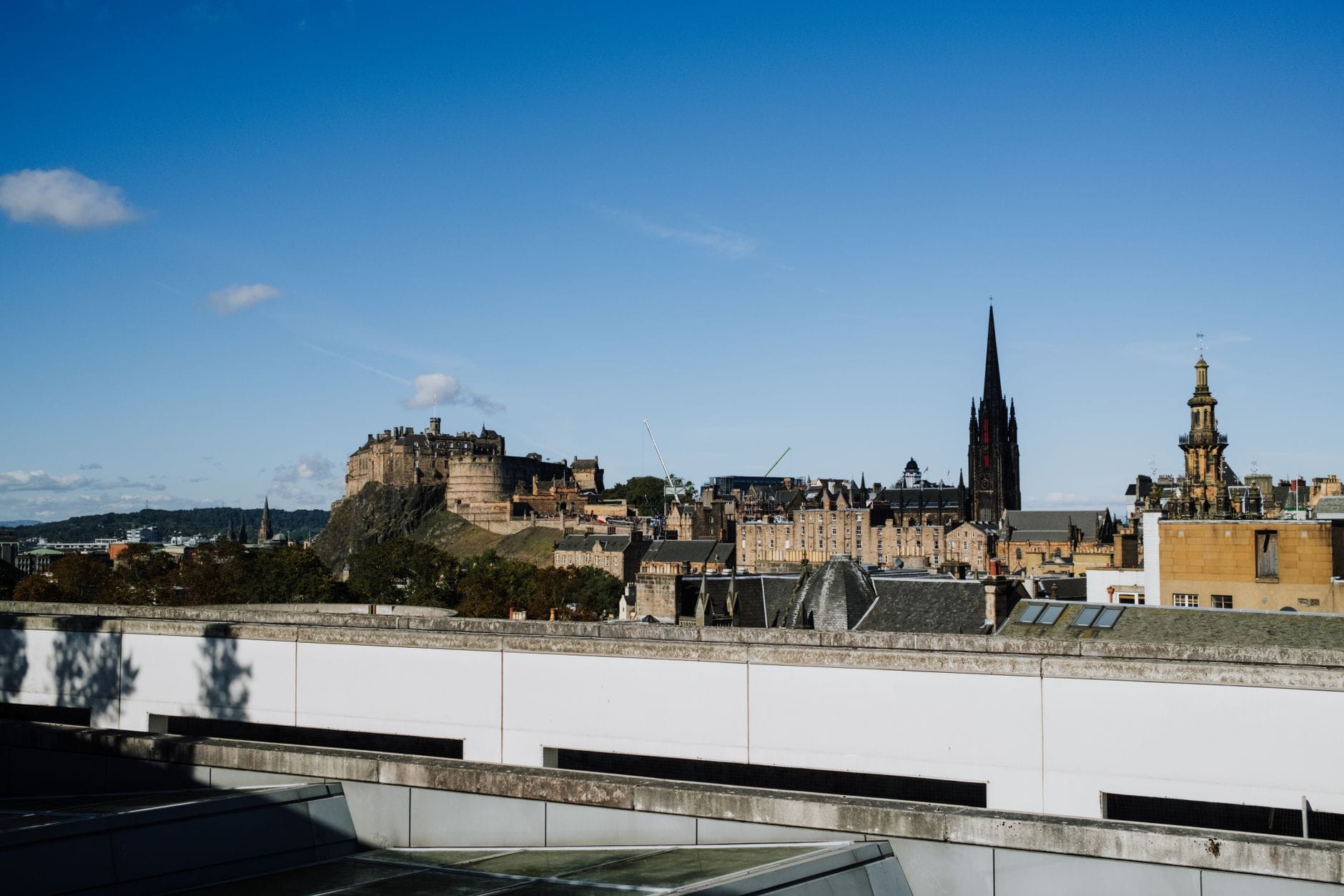 Panorama Edynburga z Edinburgh Castle i historycznymi budynkami pod bezchmurnym błękitnym niebem, widziana z pobliskiego dachu.