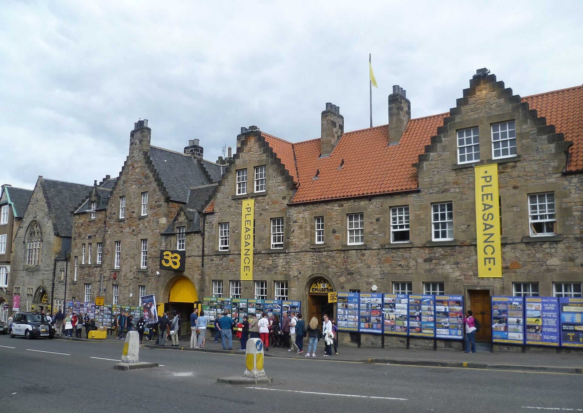 The Pleasance, jedna z głównych sal festiwalu Edinburgh Fringe, z banerami, tłumami i plenerową sygnalizacją festiwalową wzdłuż historycznego kamiennego budynku.