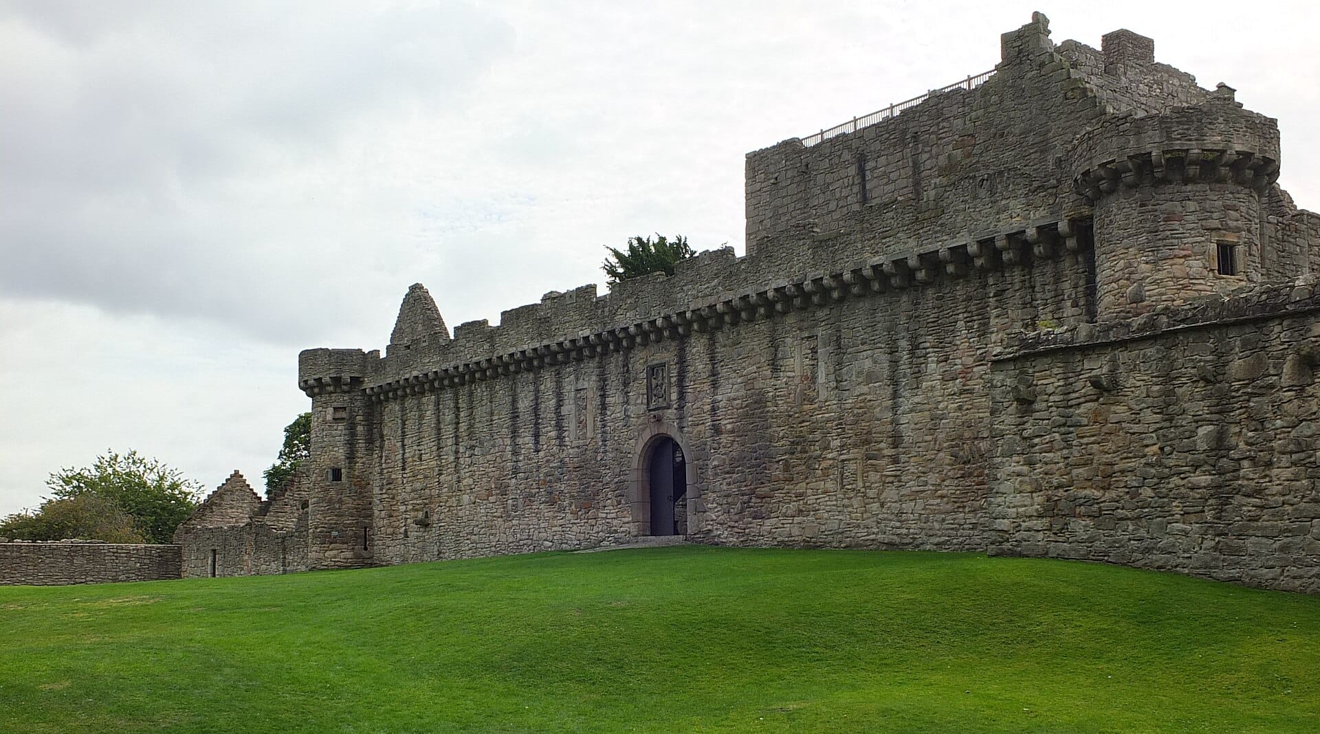 Landschaftsansicht der Steinmauern und des Eingangstors von Craigmillar Castle mit grünem Gras im Vordergrund.