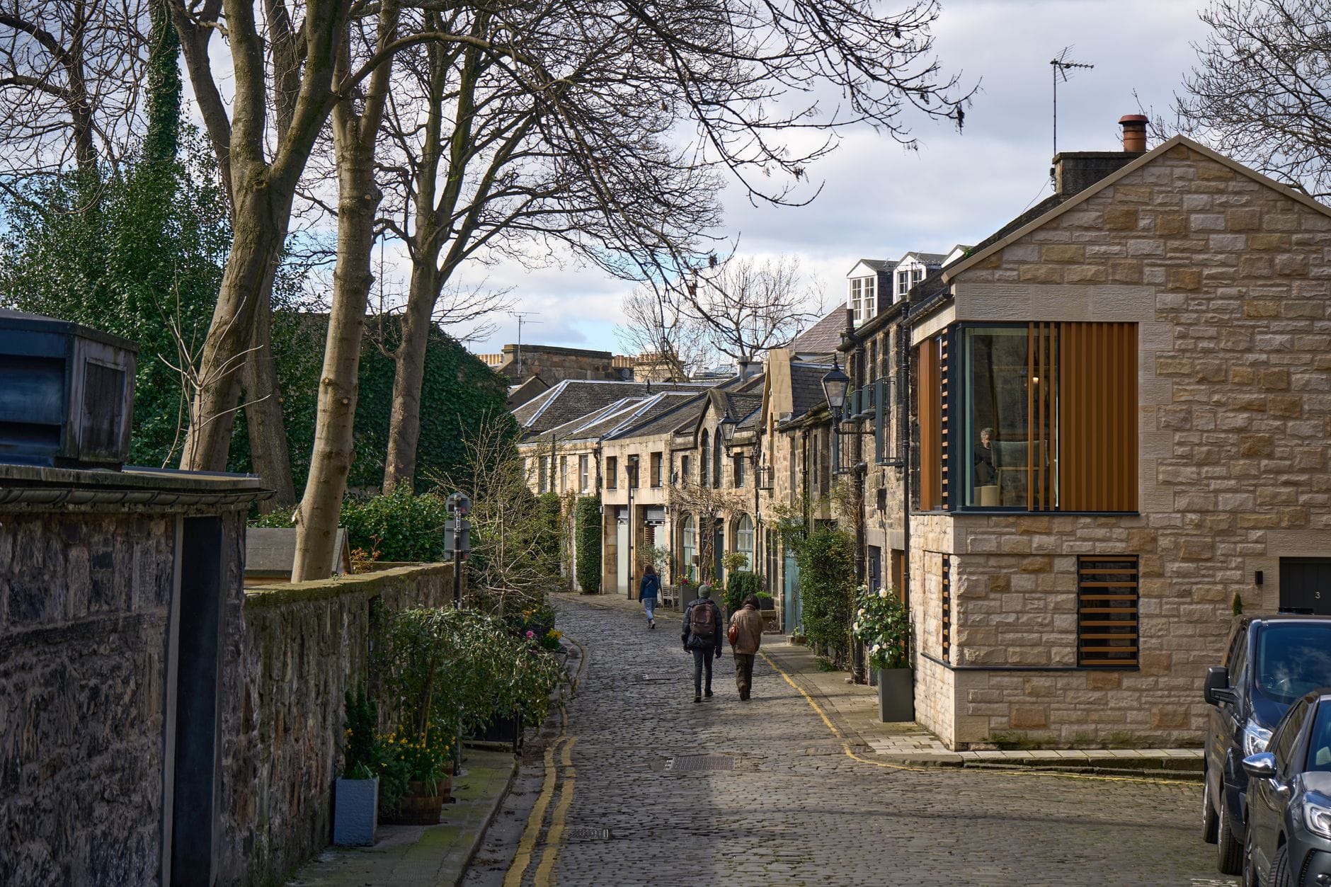 Eine ruhige, gepflasterte Wohnstraße in einem Viertel von Edinburgh mit Steinhäusern, Bäumen und zwei Personen, die unter einem blauen Himmel spazieren.