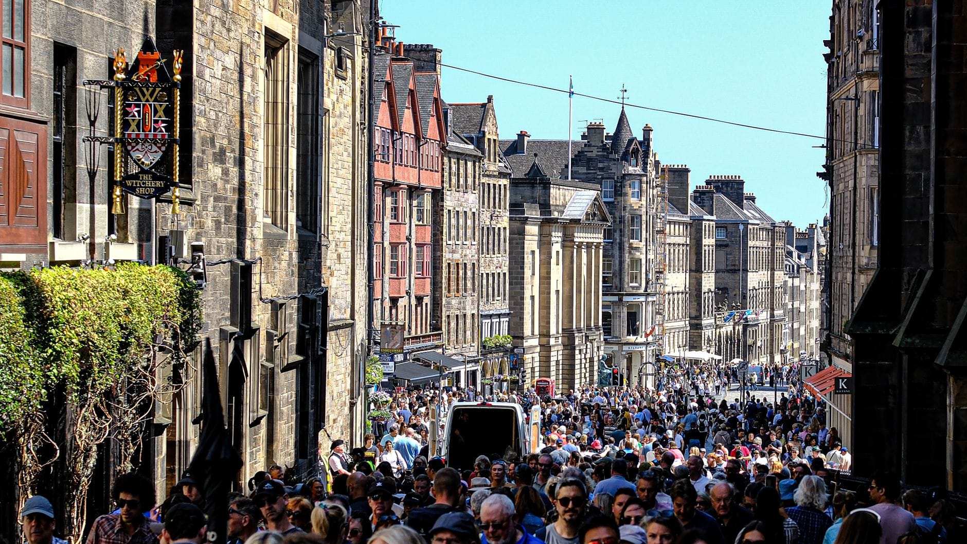 Eine belebte Royal Mile in Edinburgh, vollgepackt mit Menschenmassen an einem sonnigen Sommertag während der Festivalsaison, historische Gebäude säumen die Straße.