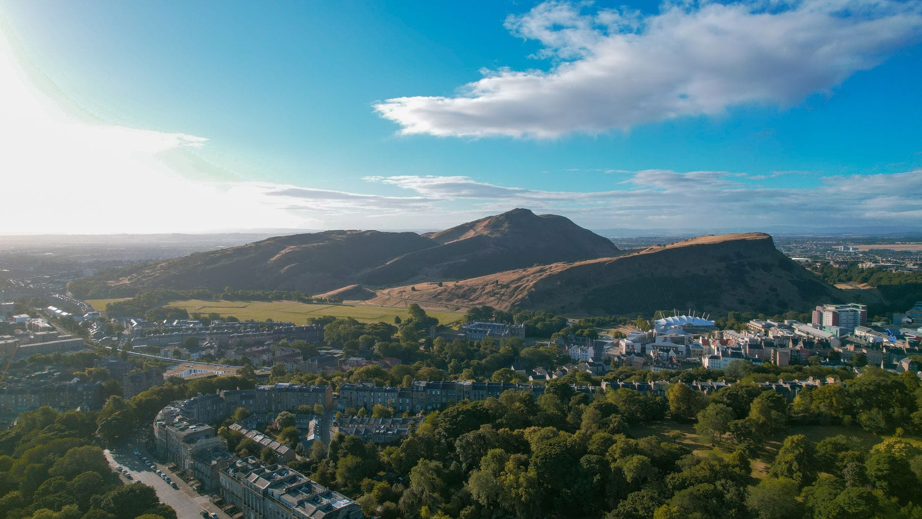 Weitläufige Landschaftsansicht des Holyrood Park und des Arthur's Seat, der an einem hellen Sommertag hinter der Stadt Edinburgh aufragt.