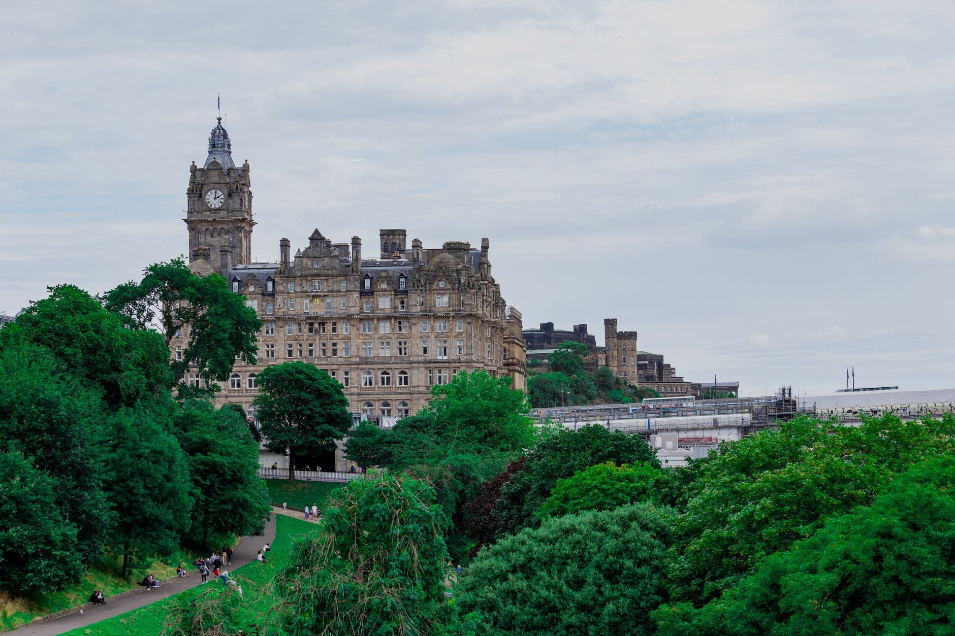 Das Balmoral Hotel, Edinburghs ikonisches 5-Sterne-Luxushotel, erhebt sich über den Princes Street zwischen grünen Bäumen und klassischer Stadtkulisse unter bewölktem Himmel.