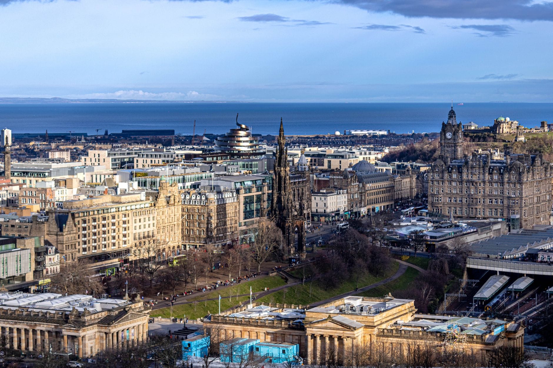 Panoramablick auf das Zentrum von Edinburgh mit dem Balmoral Hotel, der Princes Street und dem Scott Monument, im Hintergrund das Meer.