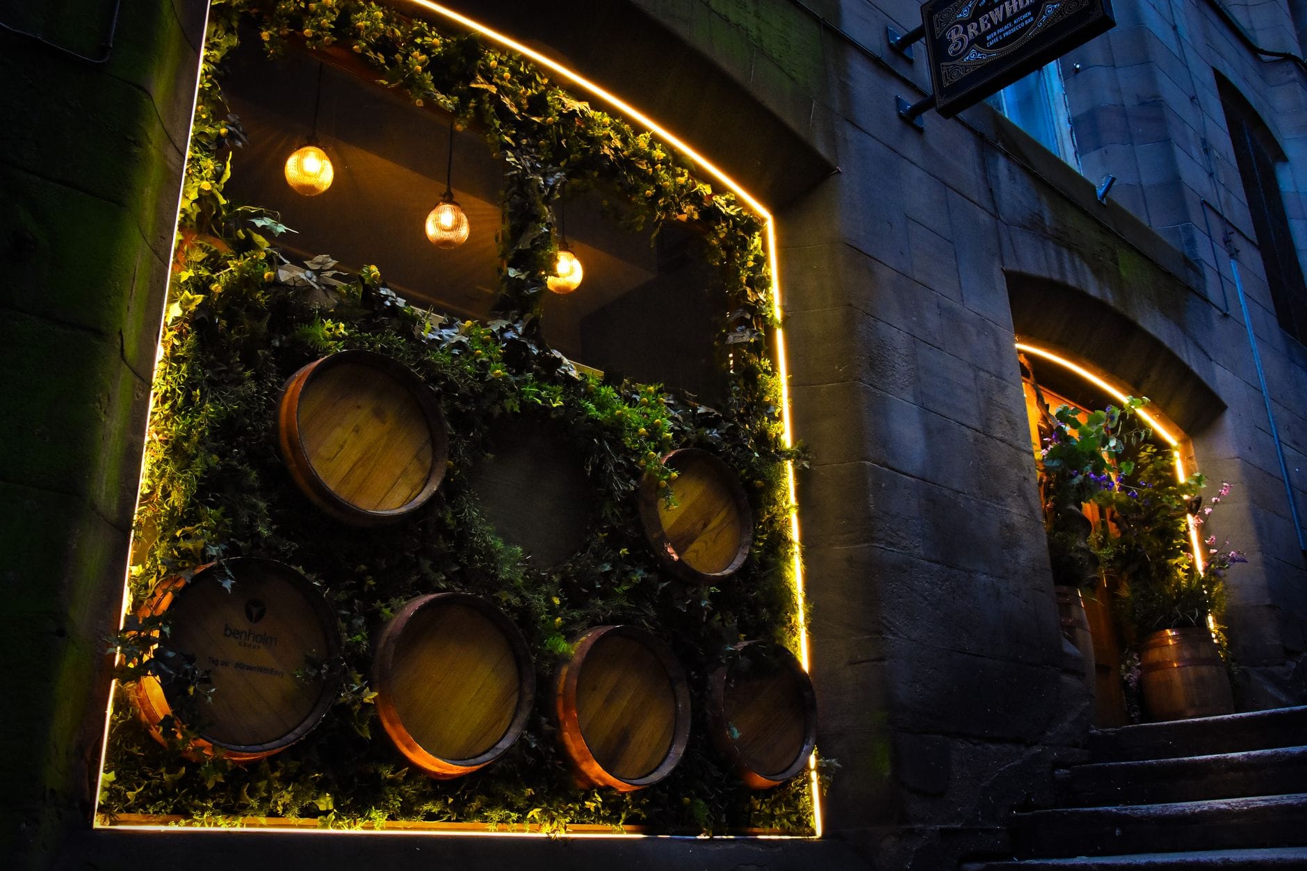 Botti di whisky illuminate esposte nella vetrina di un bar in una strada di pietra a Edinburgh di notte, con illuminazione calda.