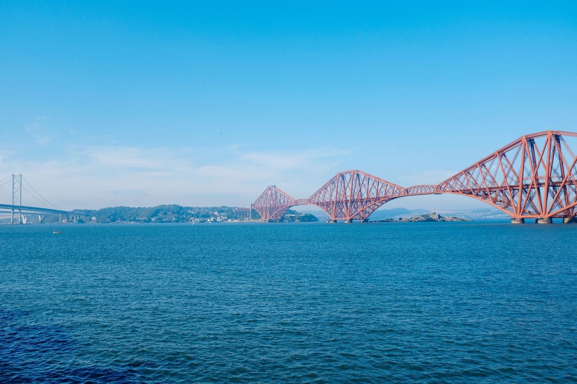 Weite Landschaftsansicht der Forth Bridges bei Edinburgh, mit der Straßen- und Eisenbahnbrücke über das Wasser unter einem klaren Himmel.