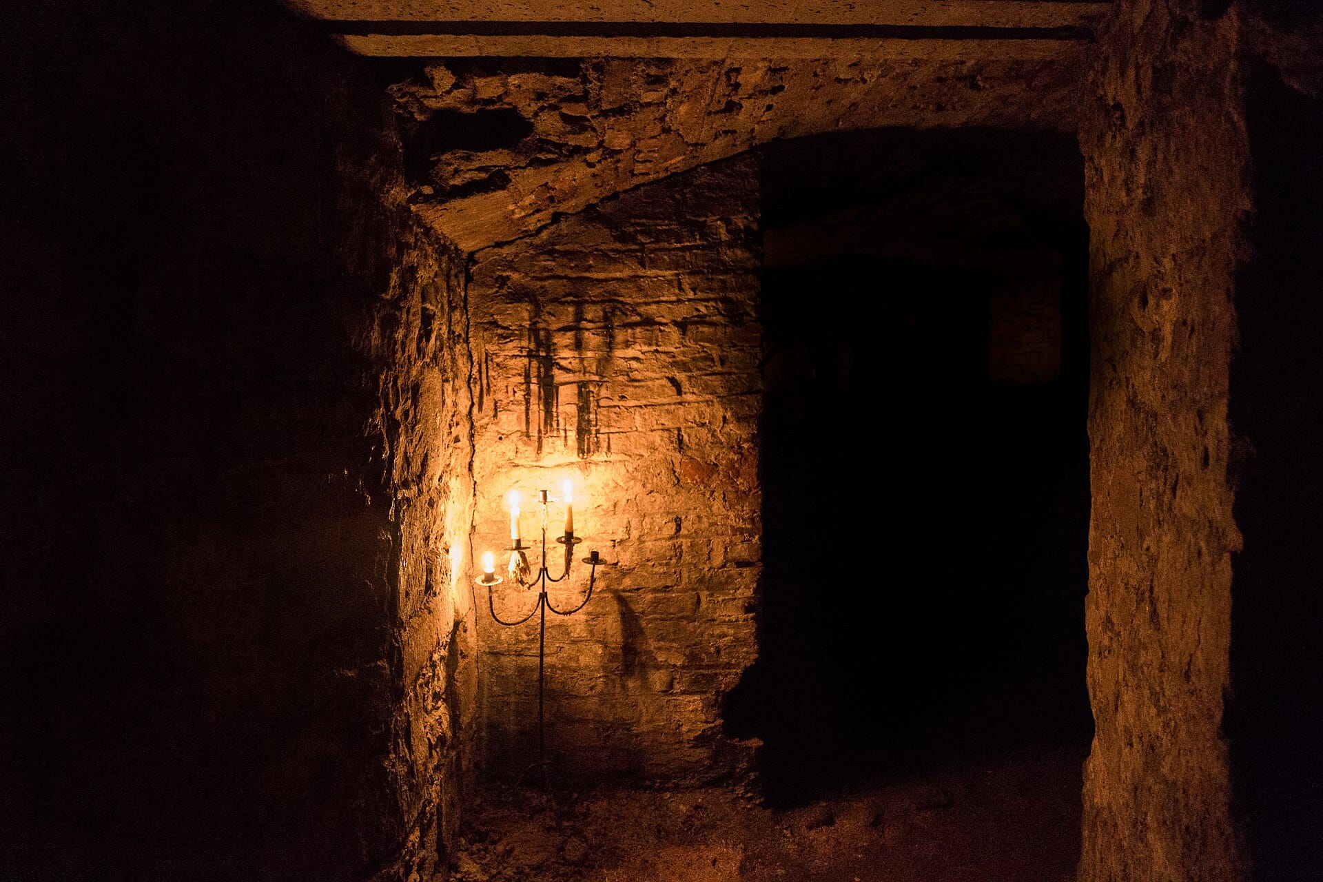 Eine schwach beleuchtete Steinkammer in den Edinburgh Vaults mit einem Gewölbebogen und einem Kerzenleuchter, der warmes Licht auf die rauen Wände wirft.