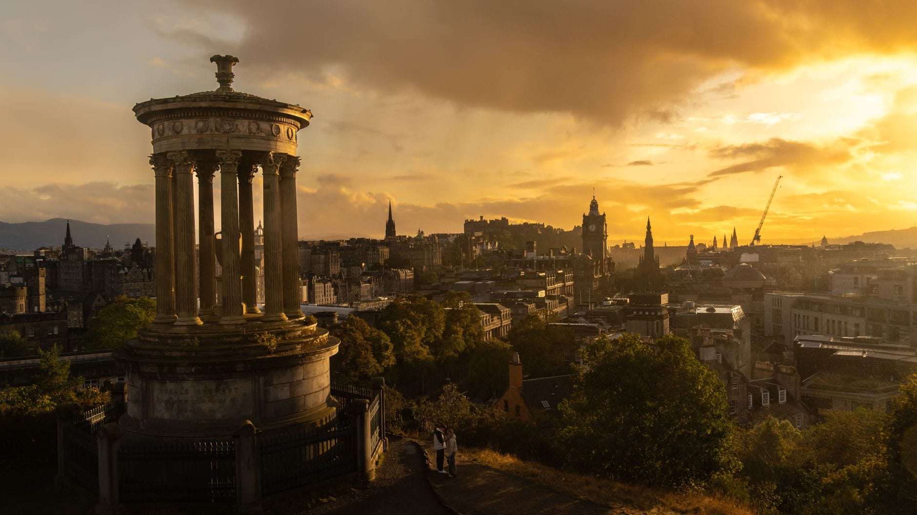 Calton Hill Denkmal mit Blick auf die Skyline von Edinburgh zur goldenen Stunde mit Schloss, Uhrturm und dramatischem Sonnenuntergangshimmel