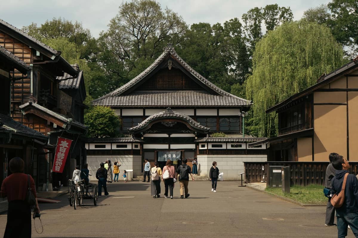 Entrance street of Edo-Tokyo Open-Air Architectural Museum with historic Japanese buildings and groups of visitors walking and exploring the area.