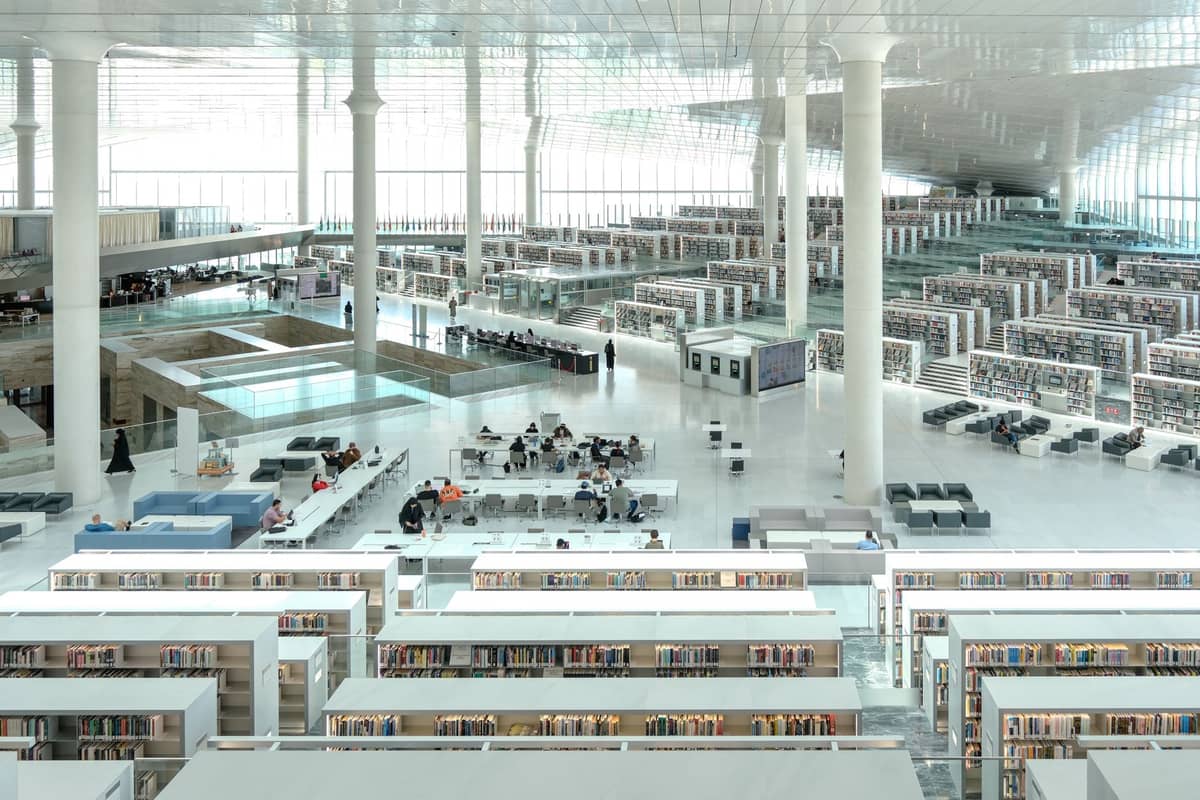Weitläufige Innenansicht der Nationalen Bibliothek Katars in Education City mit moderner Architektur, hohen Fenstern, Bücherregalen und Menschen, die in einem hellen, luftigen Raum lesen.