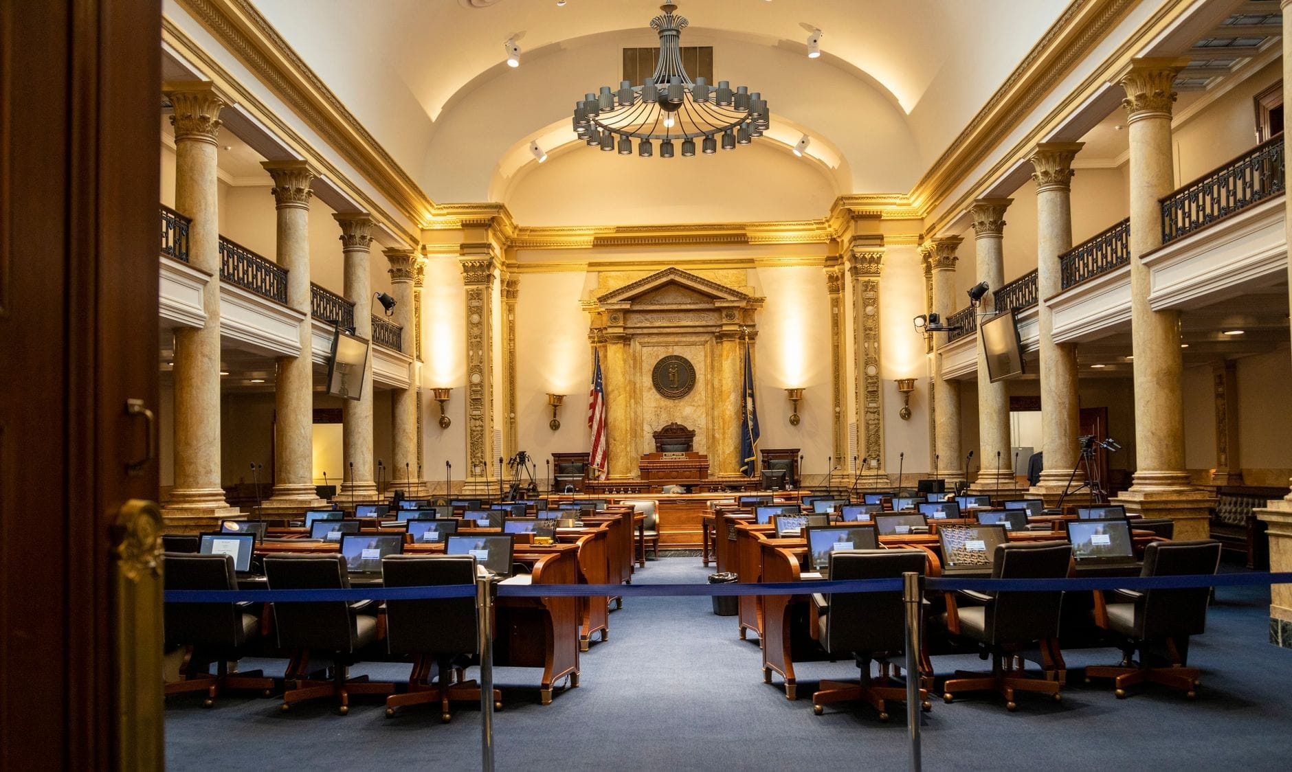 Ampia ed elegante aula legislativa con banchi e sedie, colonne classiche, soffitto alto e bandiere americane, che evoca l'atmosfera del Senato degli Stati Uniti.