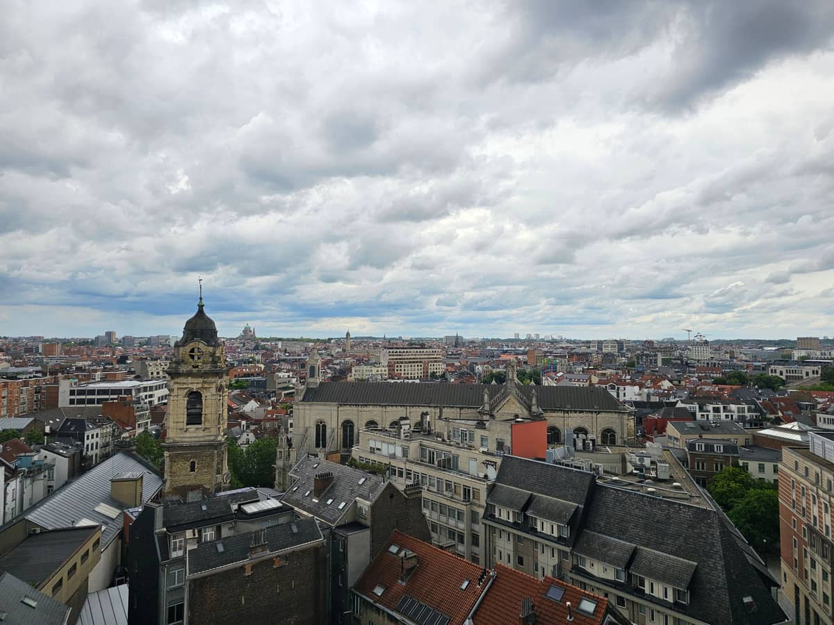 Vista ampla da Église Saint-Jean-Baptiste au Béguinage em Bruxelas, mostrando a igreja e seu icônico campanário entre os telhados da cidade.