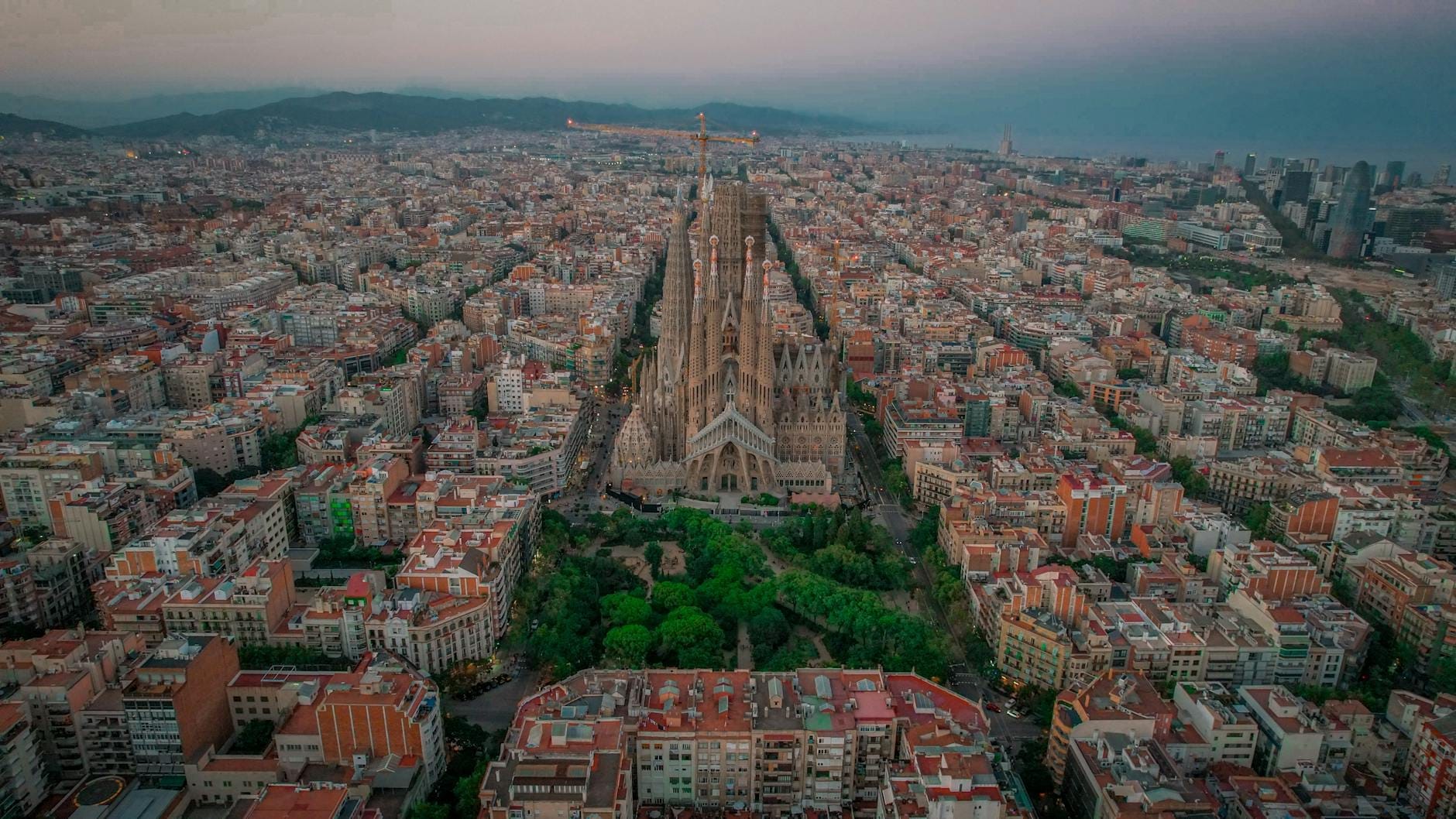 Aerial view of Barcelona's Eixample district showcasing its geometric grid layout and the Sagrada Familia surrounded by modernista buildings at dusk.