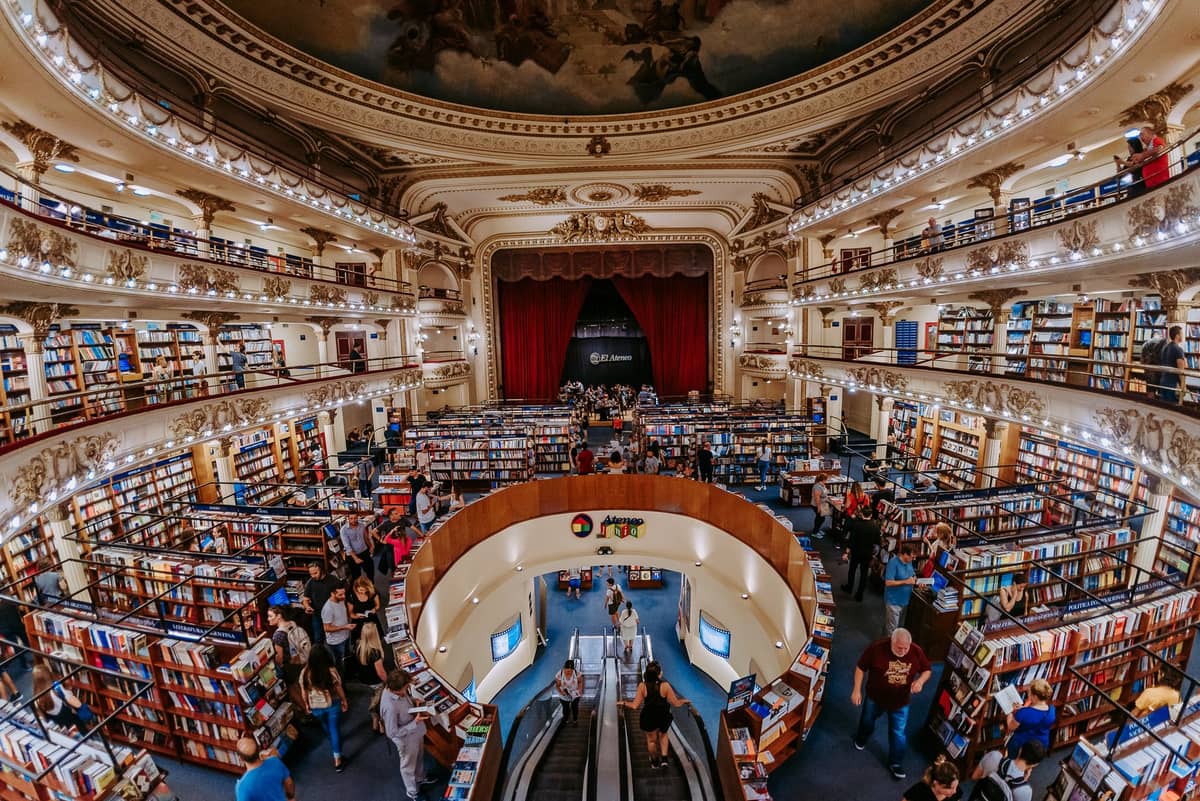 วิวภายในกว้างของ El Ateneo Grand Splendid เห็นระเบียงหลายชั้น เพดานประดับภาพเขียน ชั้นหนังสือตรงเวทีและพื้นที่เดิมของผู้ชม มีผู้เยี่ยมชมเดินเลือกหนังสือ