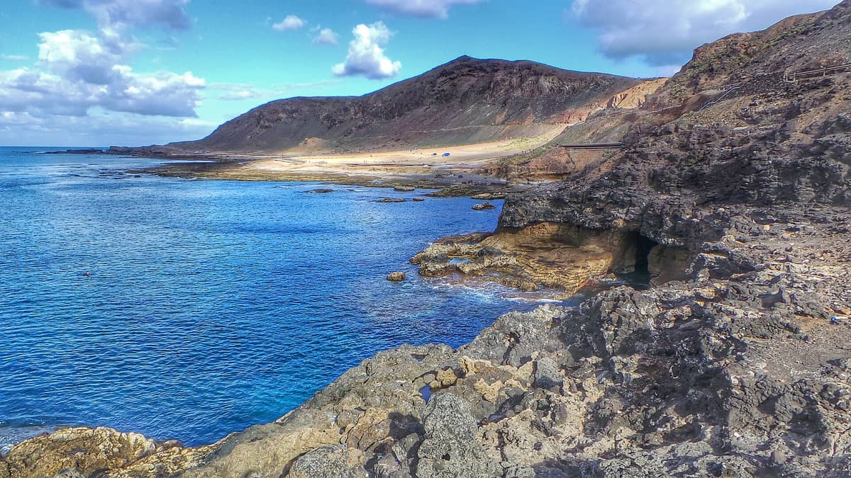 Вулканическое скалистое побережье с синими атлантическими водами, суровыми утёсами и золотистым песком в Эль-Конфиталь — на диком северном берегу Лас-Пальмаса на полуострове Ла-Ислета.