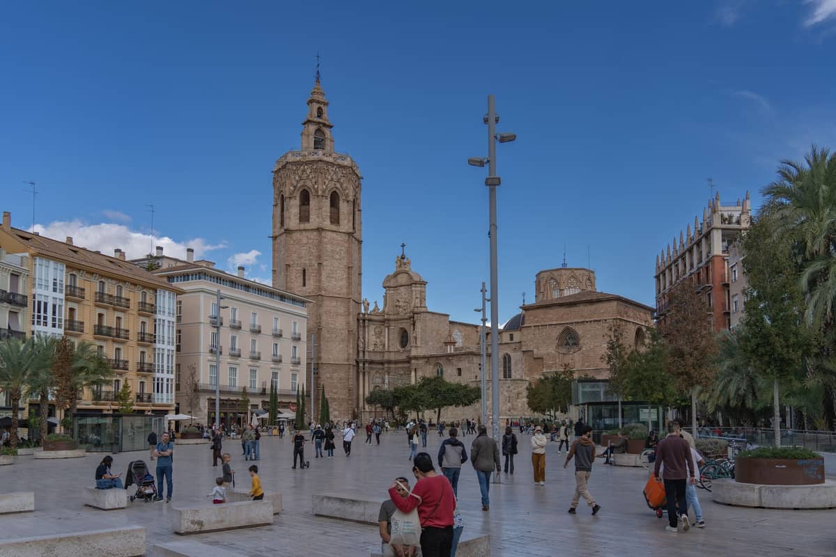 Vista ampia del campanile El Micalet che si innalza sopra la Plaça de la Reina a Valencia, con persone che passeggiano nella vivace piazza e la cattedrale sullo sfondo.