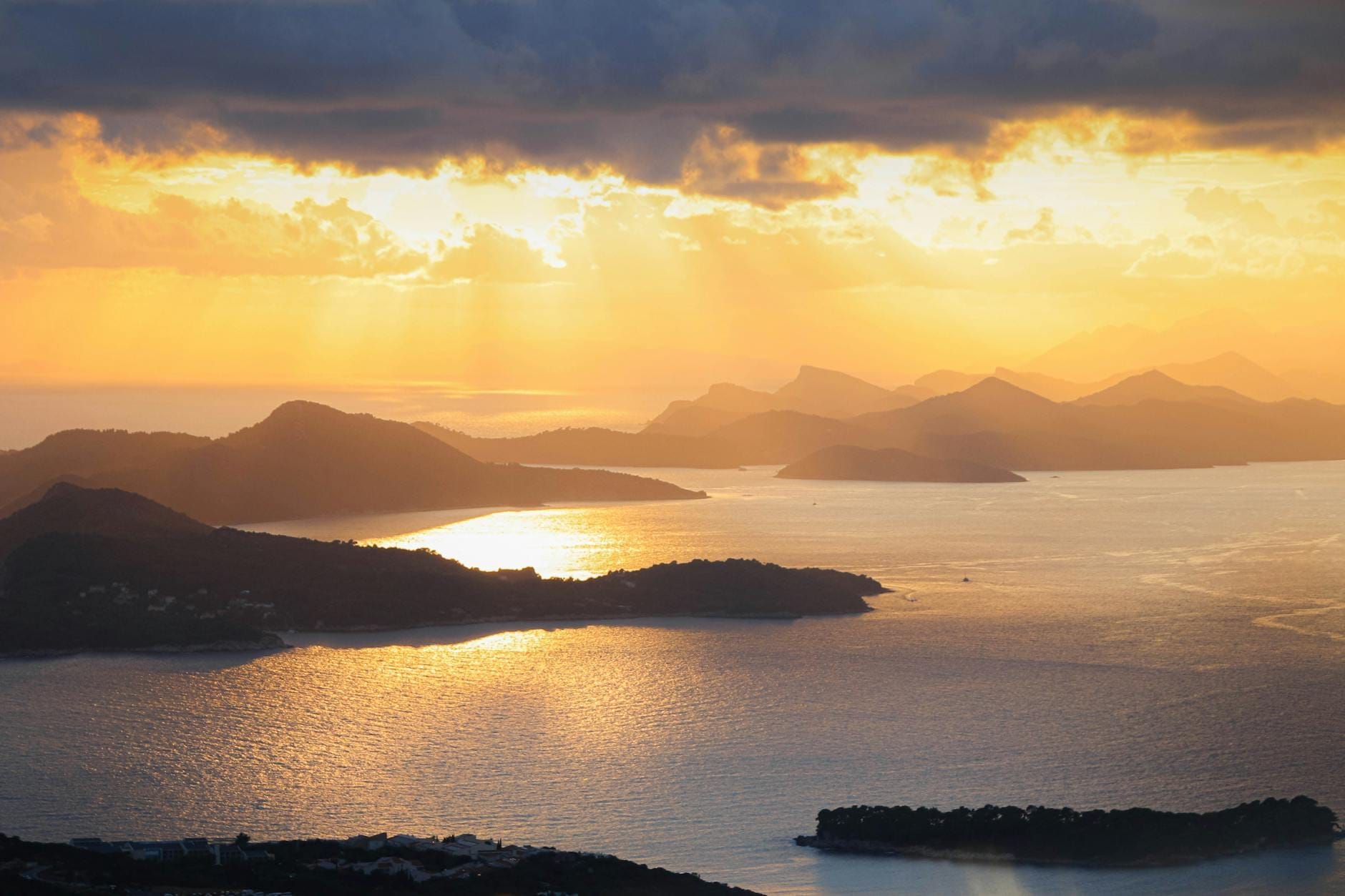 Una puesta de sol dorada sobre las islas Elafiti con nubes dramáticas, un mar en calma y siluetas de islas que se extienden a lo lejos.