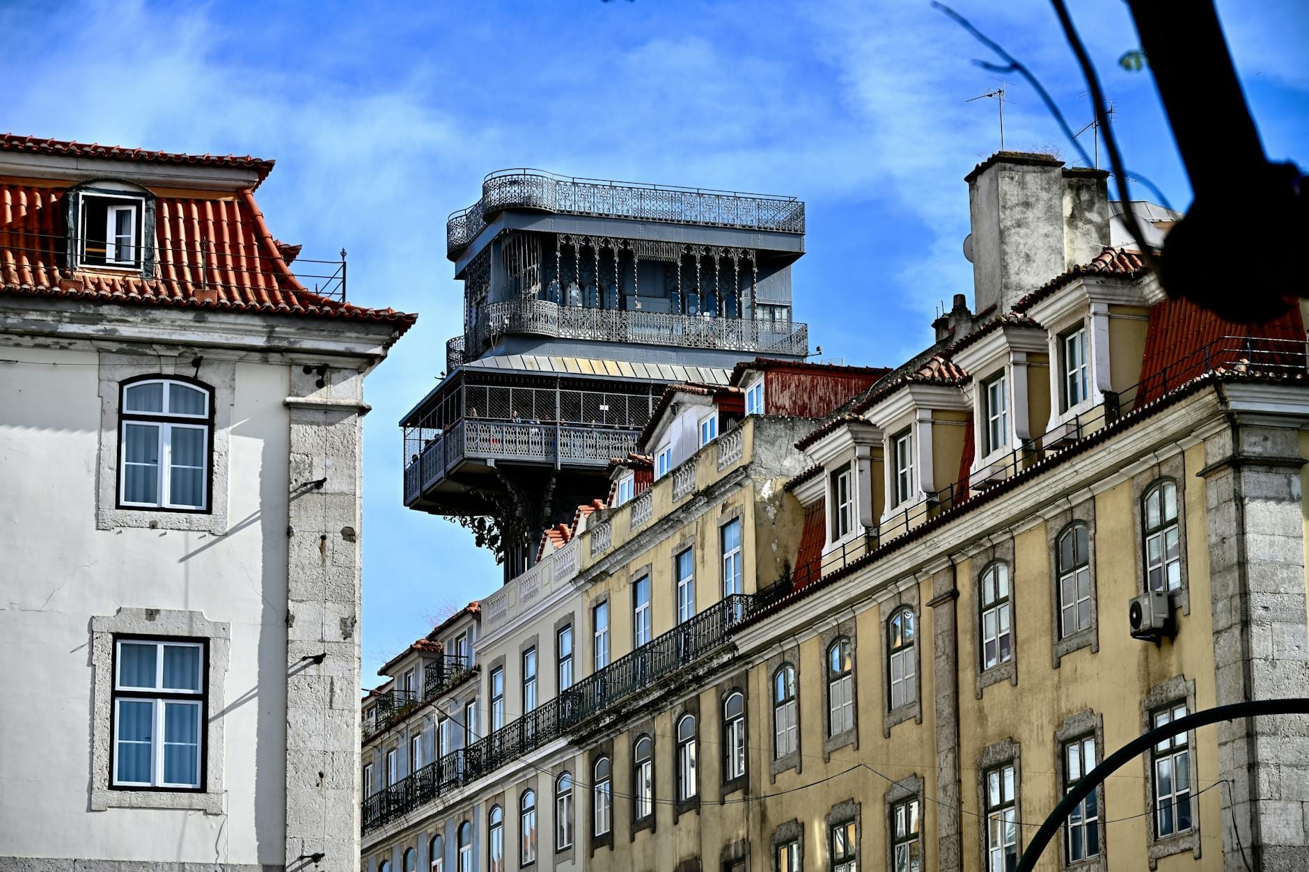 La torre in ferro dell'Elevador de Santa Justa si erge sopra gli edifici storici di Lisbona sotto un cielo azzurro, con la sua struttura neogotica al centro della città.