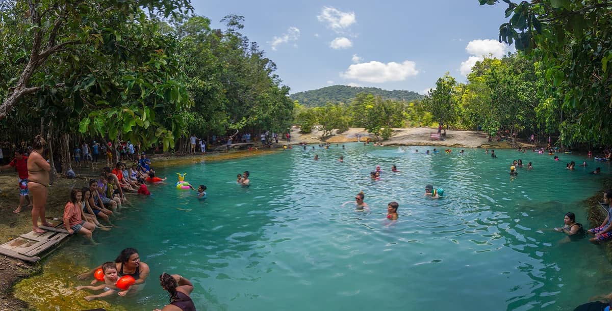 Familien und Touristen schwimmen und entspannen sich an den türkisfarbenen Ufern des Emerald Pool, umgeben von üppiger Vegetation und fernen Hügeln in Krabi, Thailand.
