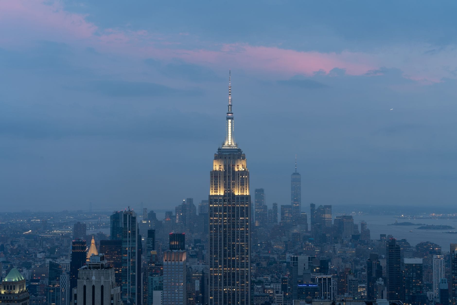 L'Empire State Building illuminato al crepuscolo, svettante sullo skyline di Midtown Manhattan con le luci della città e un cielo drammatico tra il blu e il rosa sullo sfondo.
