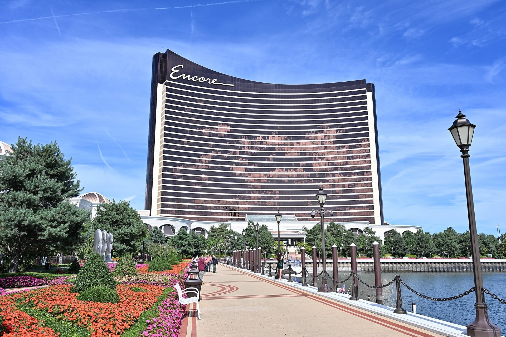 Il lussuoso hotel Encore Boston Harbor si erge dietro giardini colorati e una passeggiata lungo il fiume Mystic sotto un cielo azzurro limpido.