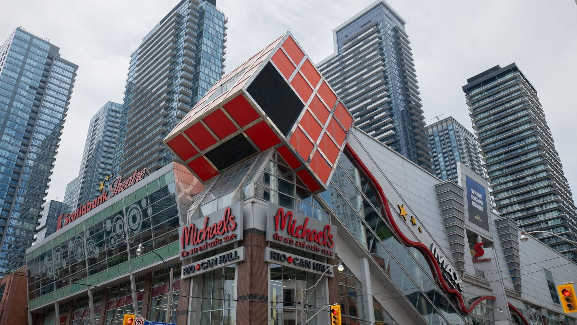 วิวถนนของอาคาร Scotiabank Theatre ในโตรอนโต พร้อมด้านหน้าอาคารรูปทรงลูกบาศก์สีแดงขนาดยักษ์ ล้อมรอบด้วยคอนโดมิเนียมสูงทันสมัยภายใต้ท้องฟ้ามีเมฆในย่าน Entertainment District ของโตรอนโต