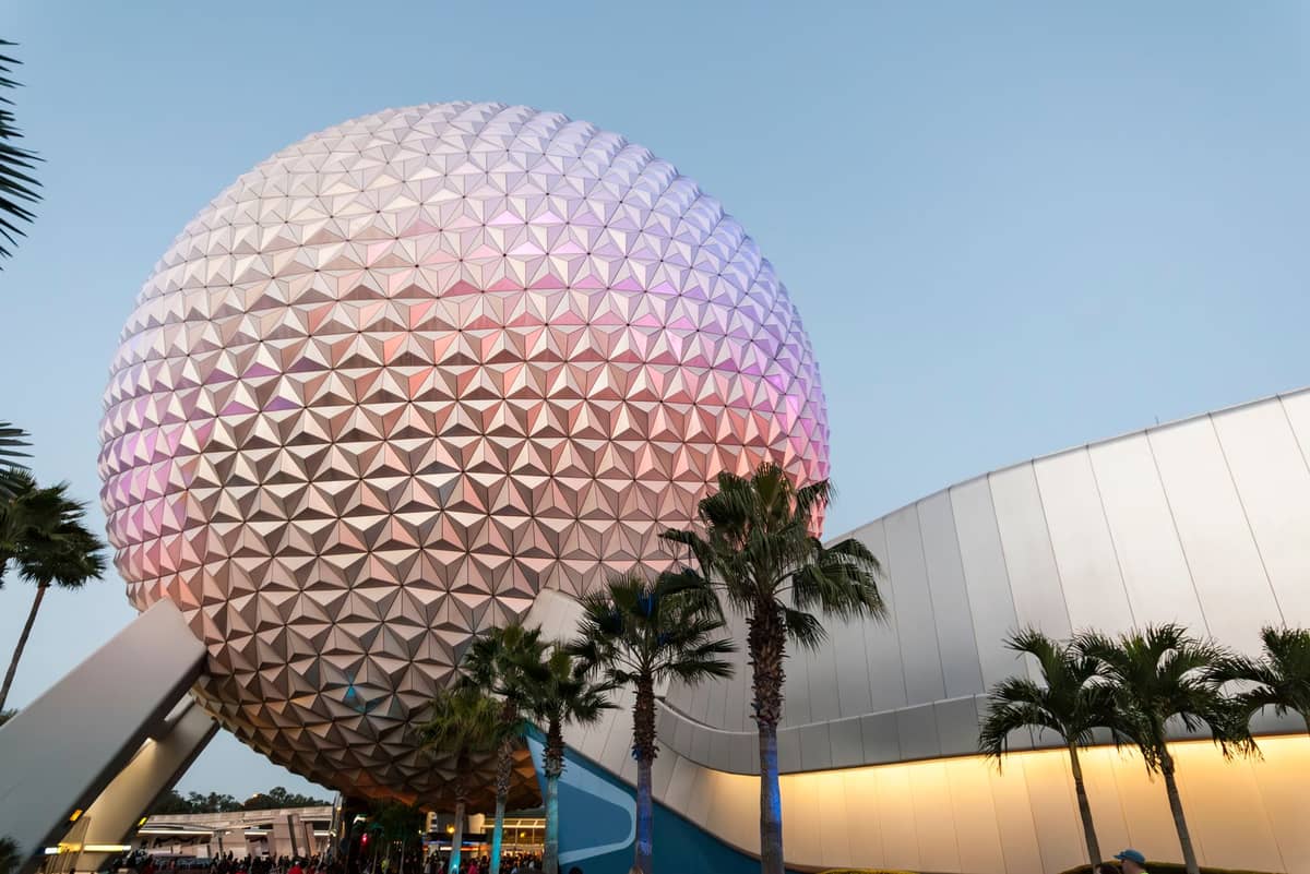 The iconic geodesic dome of Spaceship Earth at EPCOT, photographed at dusk with a clear sky and palm trees in the foreground.