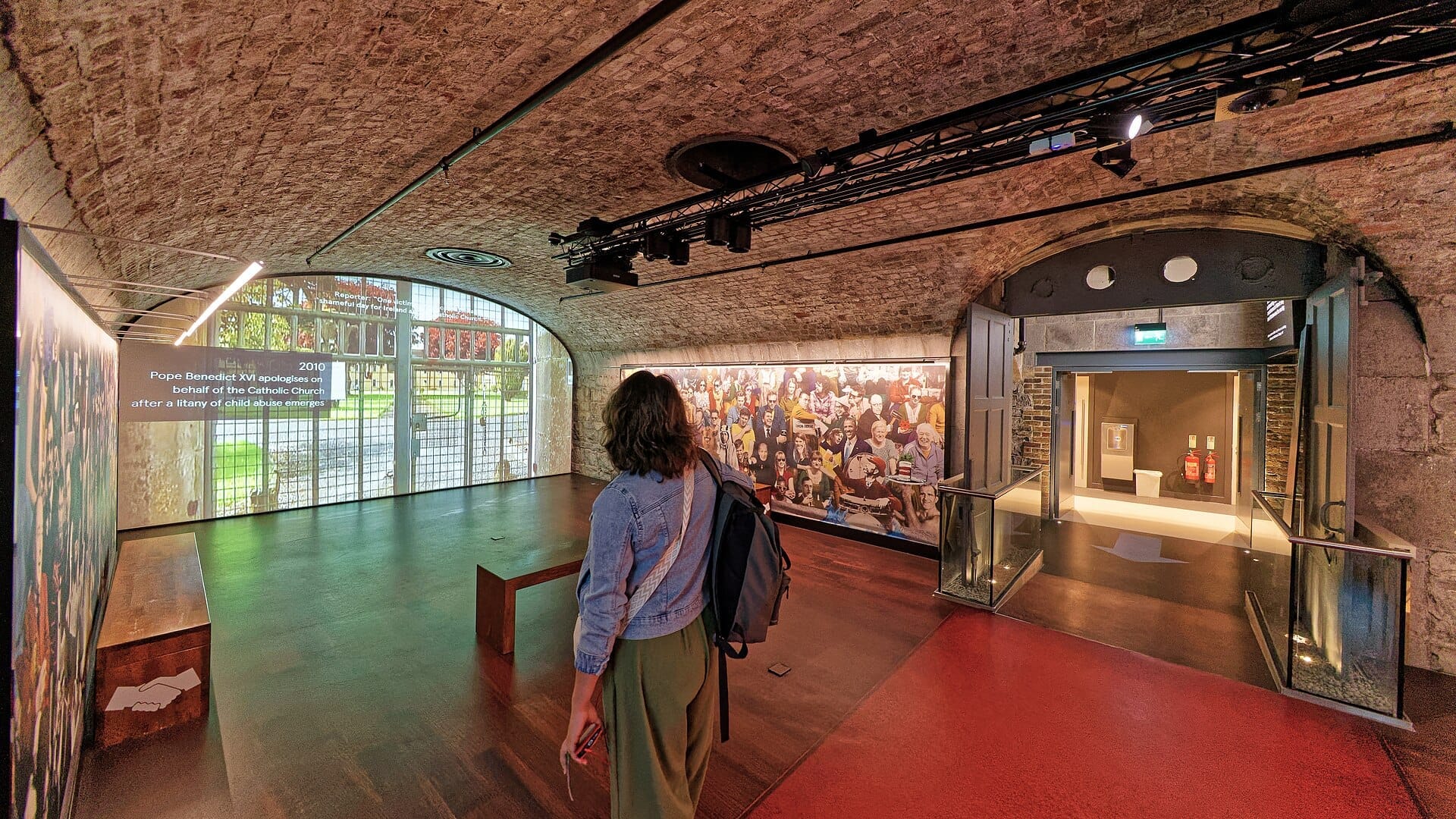 Un visitatore che cammina attraverso l'interno a volta in pietra dell'EPIC The Irish Emigration Museum, con esposizioni e proiezioni storiche visibili.
