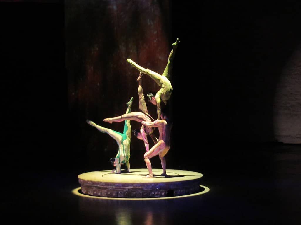 Vier ERA-Akrobaten halten unter einem Scheinwerfer auf einer runden Plattform im Shanghai Circus World ein Balance-Tableau, darunter ein Handstand in zwei Ebenen.