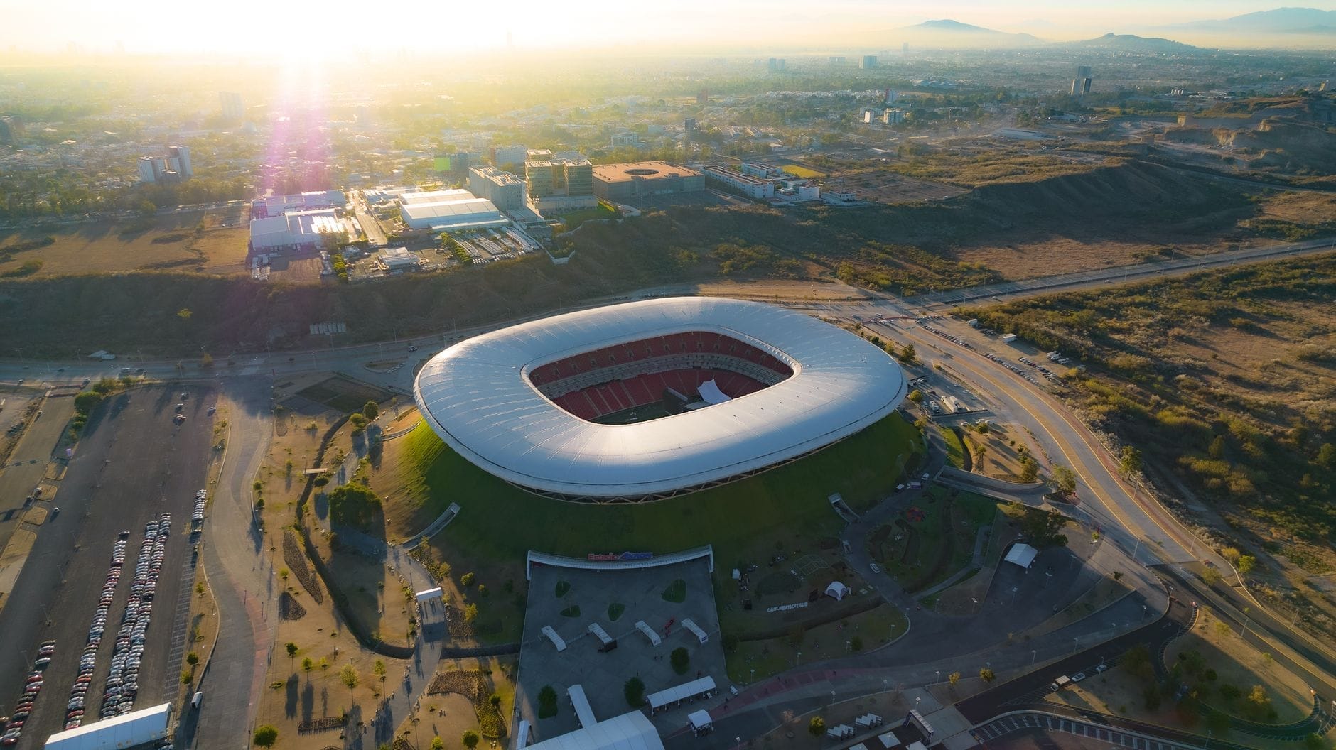 Vista aerea dell'Estadio Akron circondato dalla città al tramonto, con l'architettura moderna dello stadio e l'atmosfera vibrante che lo rendono il principale impianto calcistico di Guadalajara.