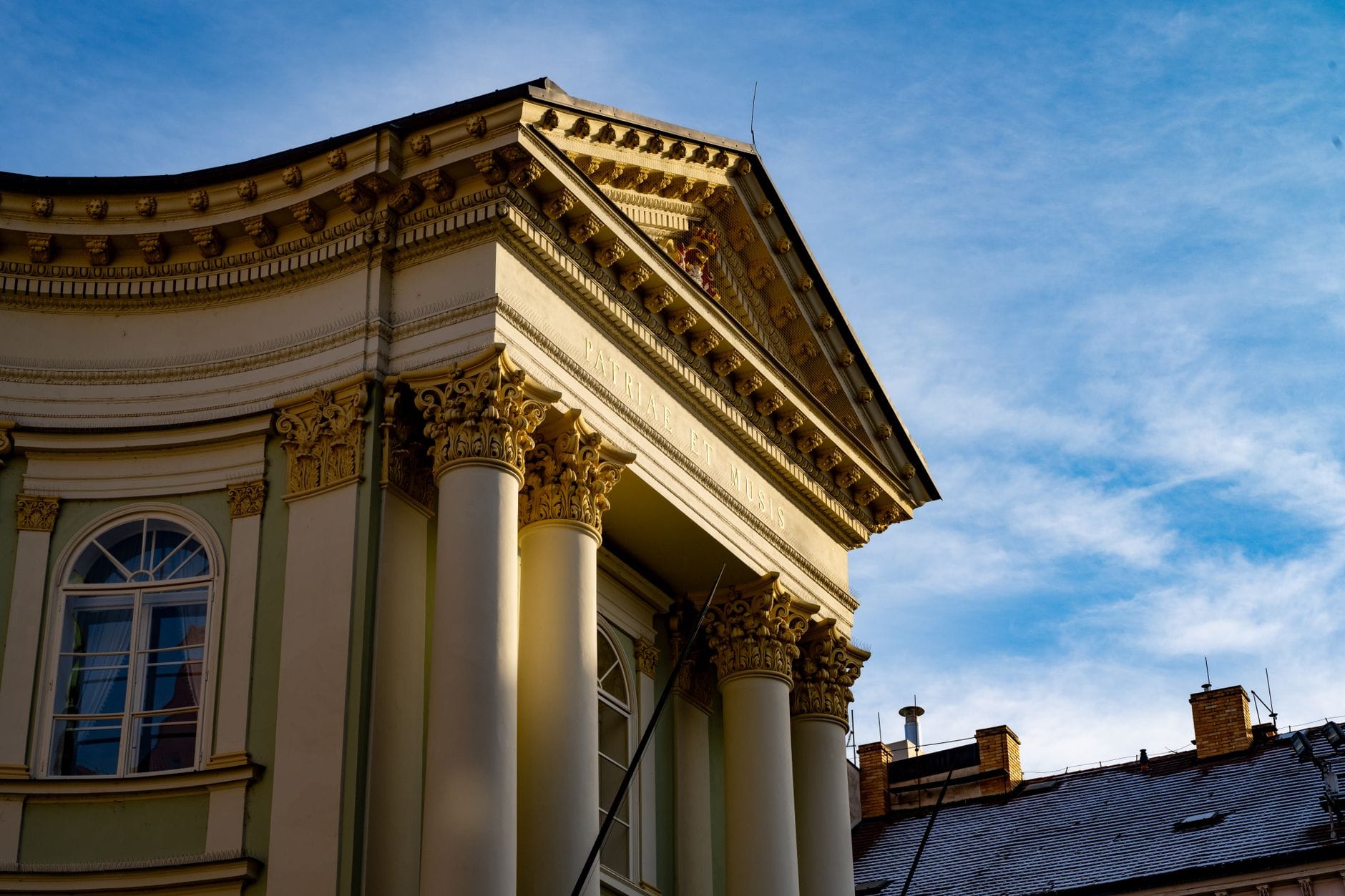 Vista ravvicinata dell'elegante facciata neoclassica del Teatro degli Stati di Praga, con colonne ornate e capitelli decorativi su sfondo di cielo azzurro.